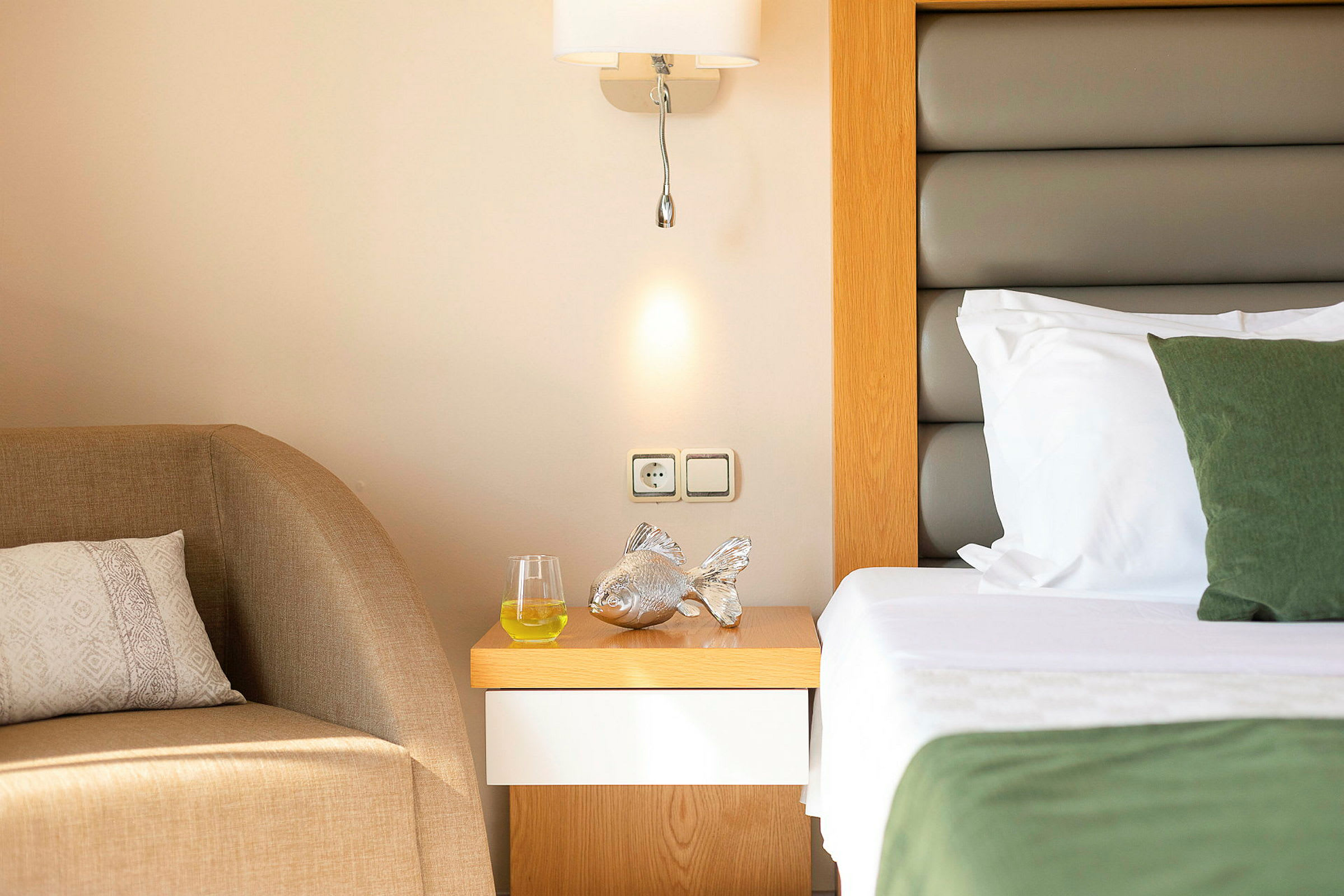 Et hotelværelse med et nærbillede af natbordet med en sølvfarvet dekoration, et glas med drik og en seng ved siden af. (AI-genereret tekst)