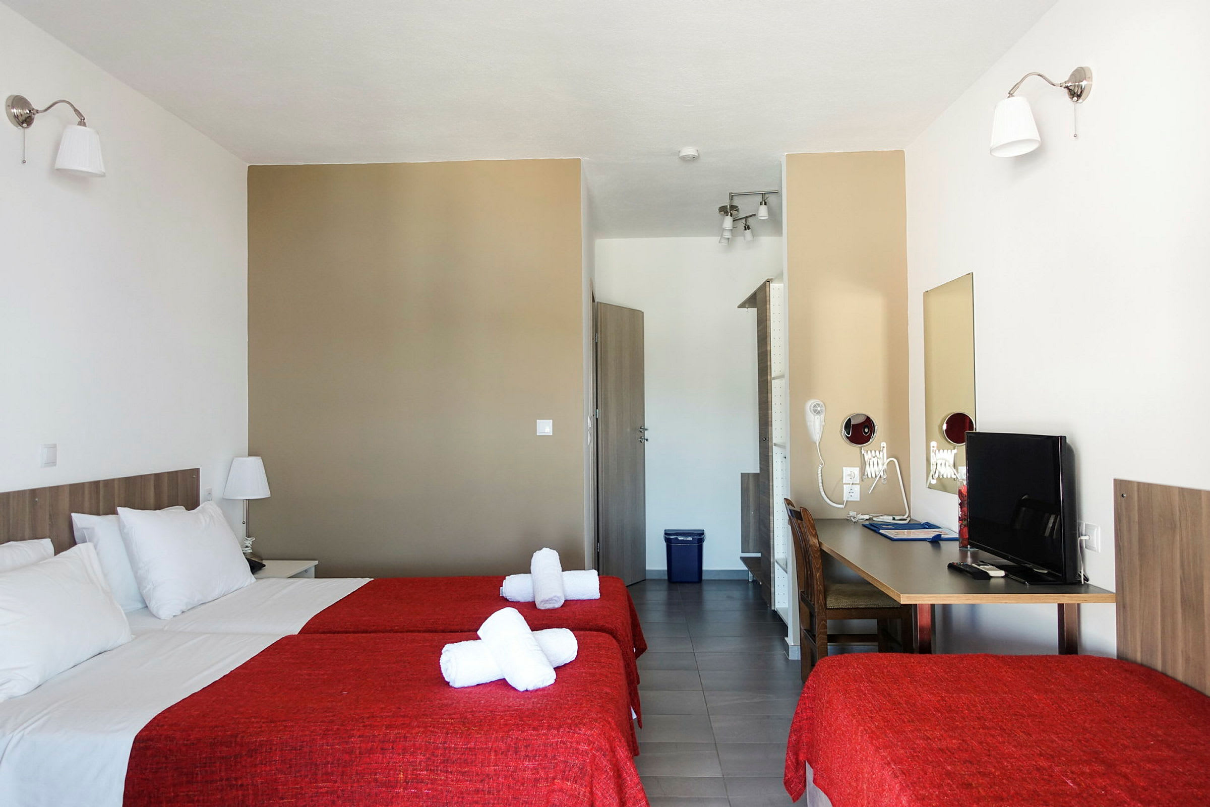 Hotelværelse med to senge og røde sengelagner. (AI-genereret tekst)