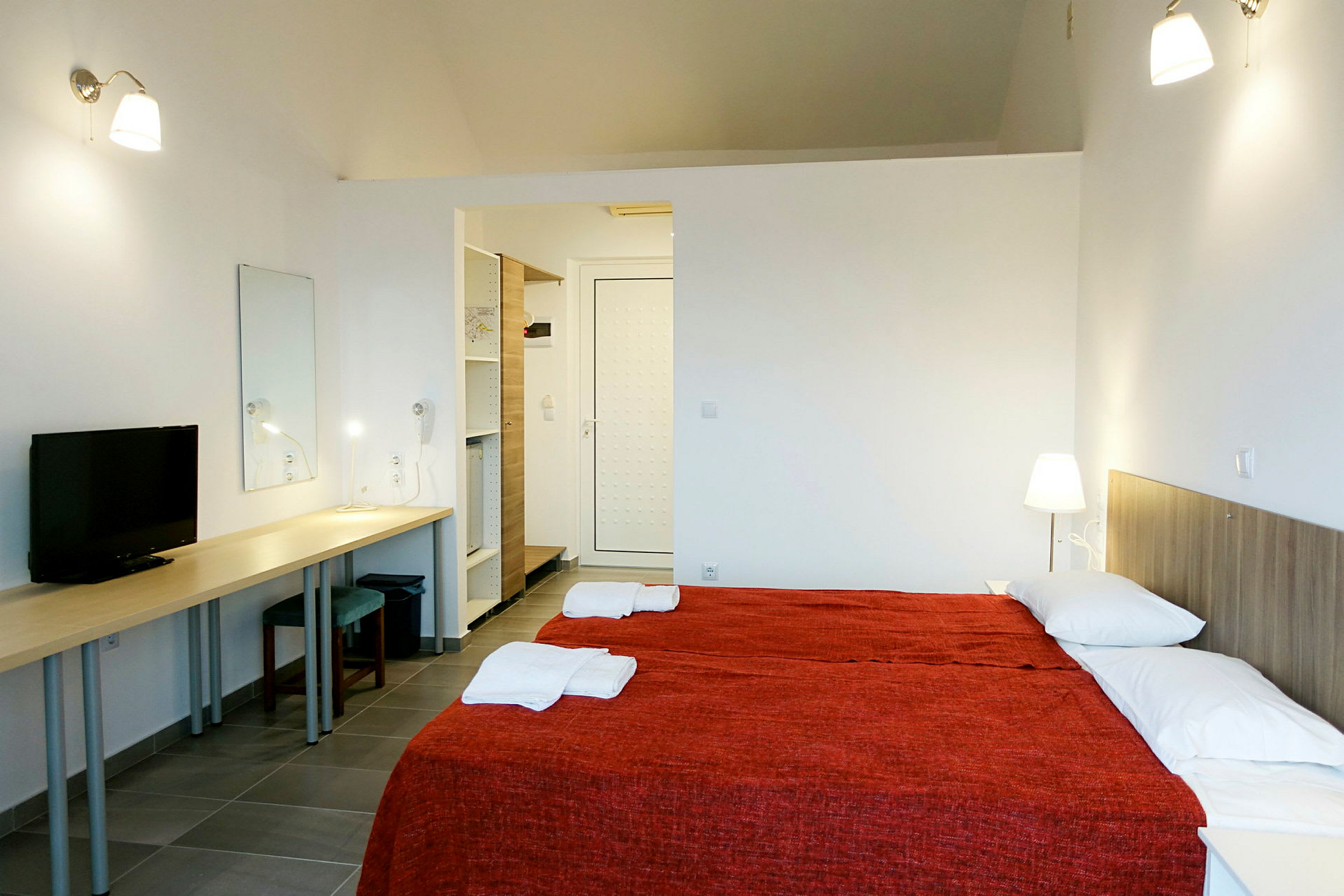 Et hotelværelse med to enkeltsenge, en lang arbejdsflade, et tv og en dør til et garderobe. (AI-genereret tekst)
