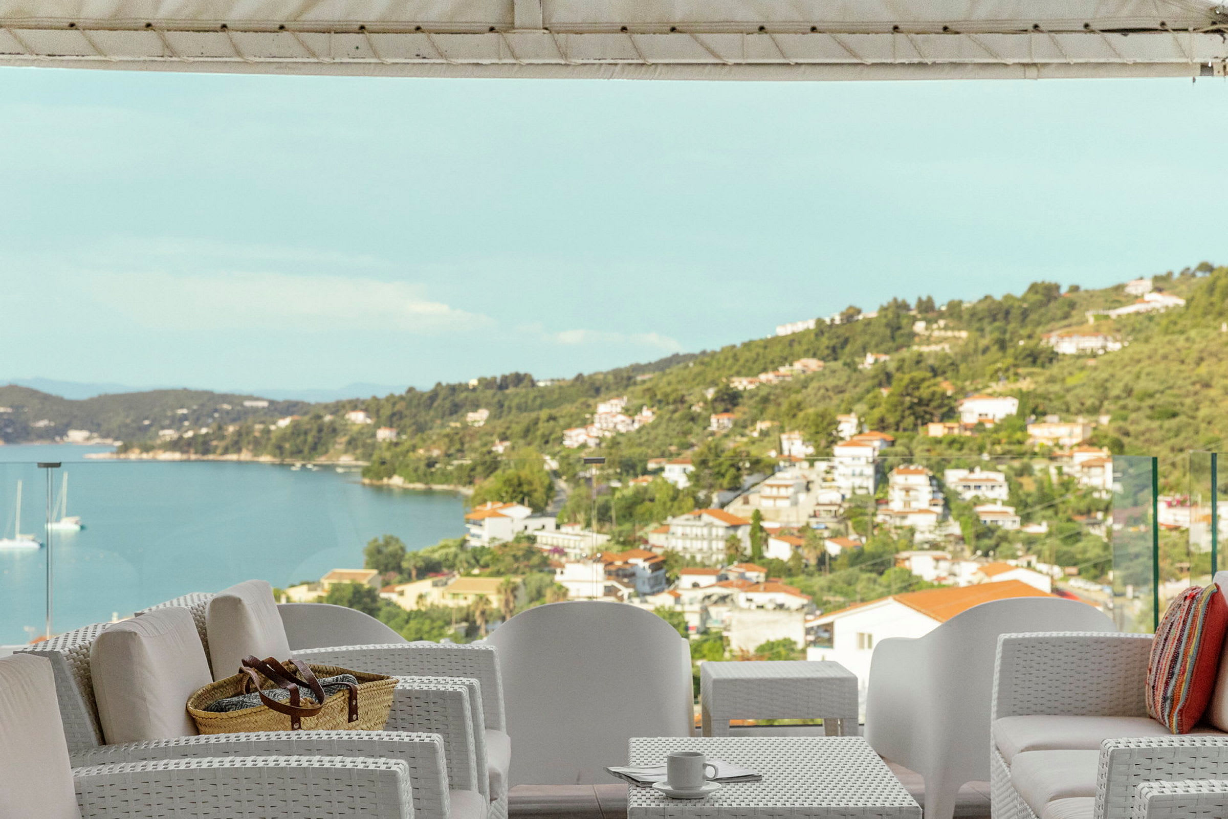 Udendørsmøbler på en terrasse med udsigt over havet og en kystby. (AI-genereret tekst)
