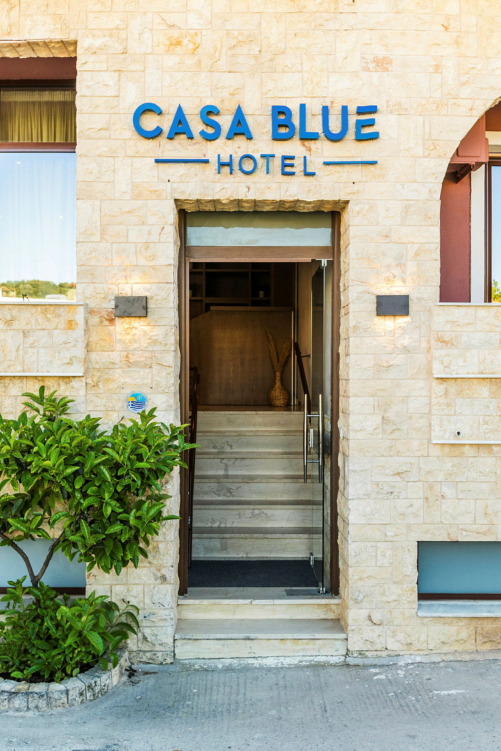 Indgangen til Casa Blue Hotel, med glasdøre og stenfacade. (AI-genereret tekst)