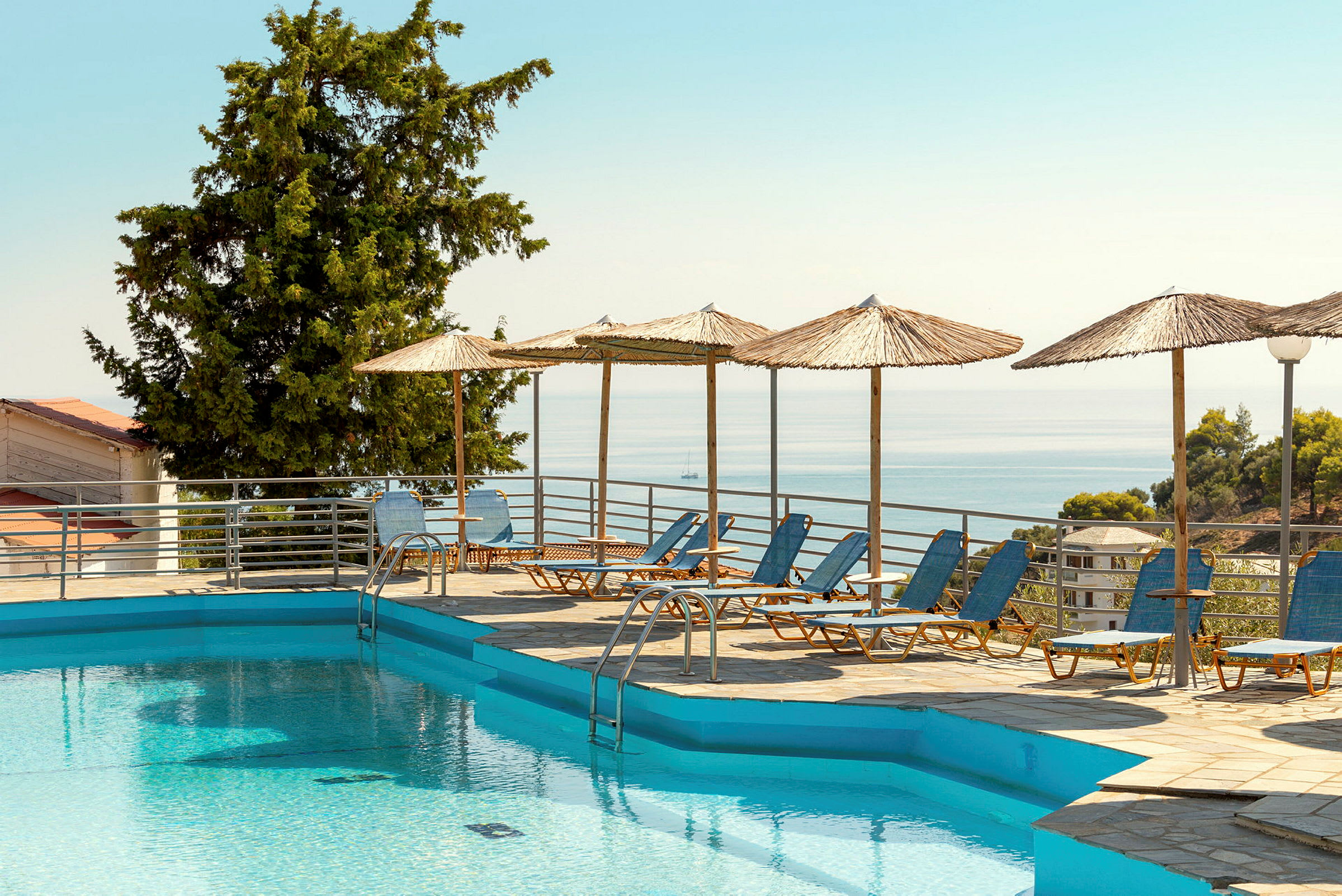 Udendørs pool med liggestole og parasoller ved havet. (AI-genereret tekst)