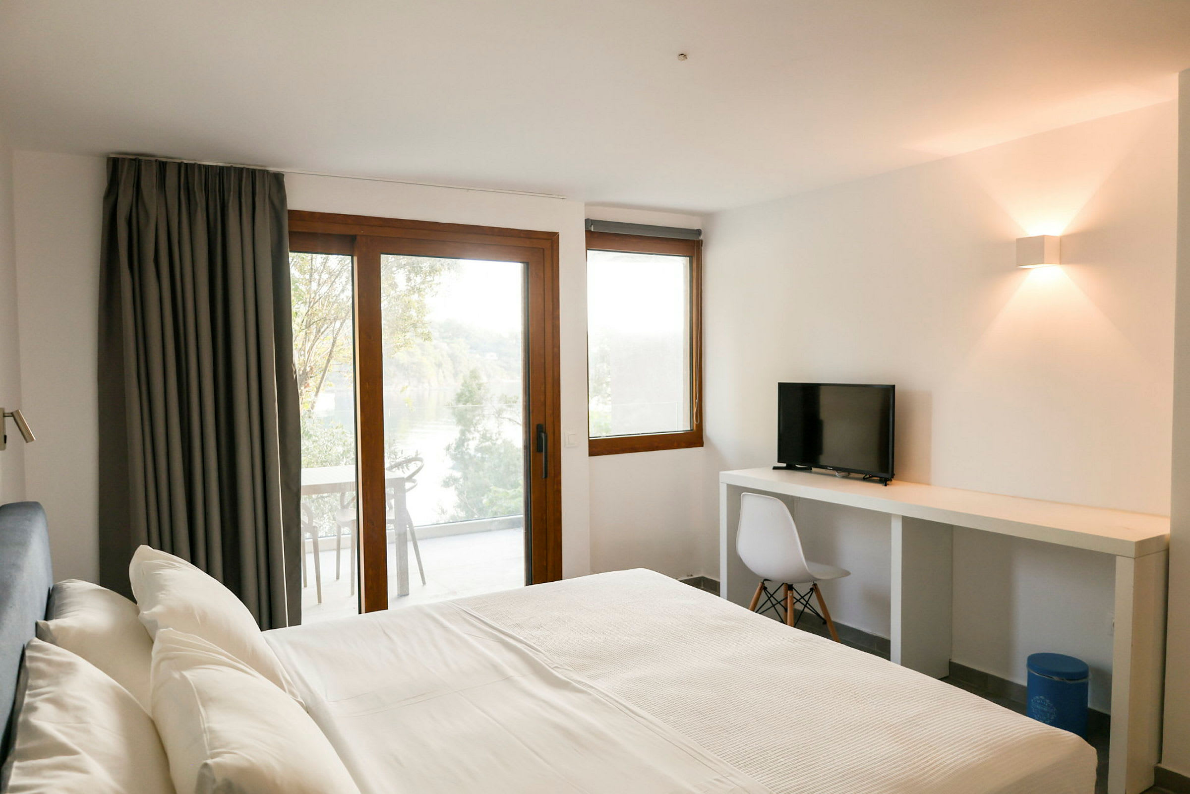 Et hotelværelse med en seng, skrivebord og stol samt balkon med udsigt. (AI-genereret tekst)