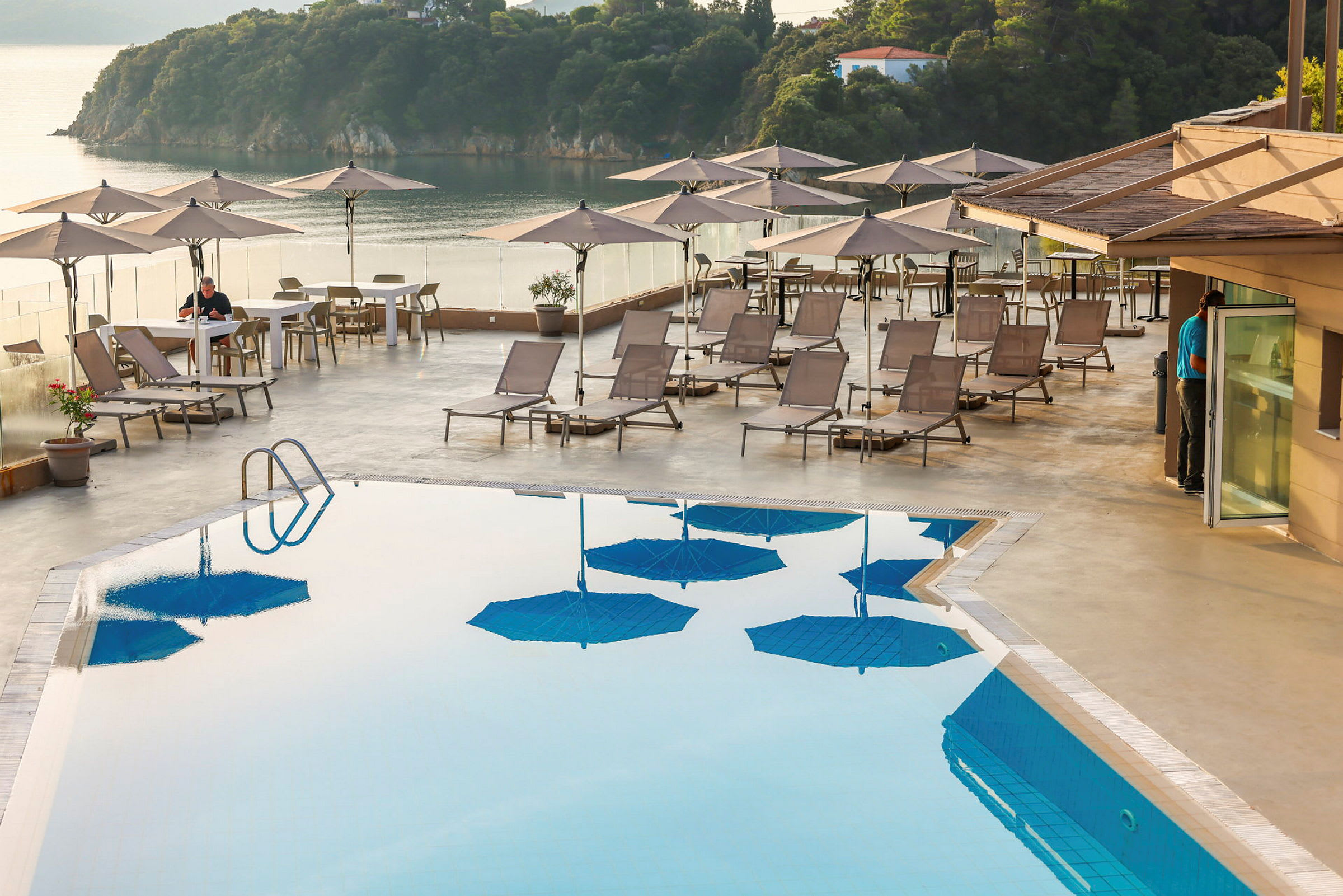 Udendørs swimmingpool med liggestole og parasoller på en terrasse med udsigt over havet. (AI-genereret tekst)