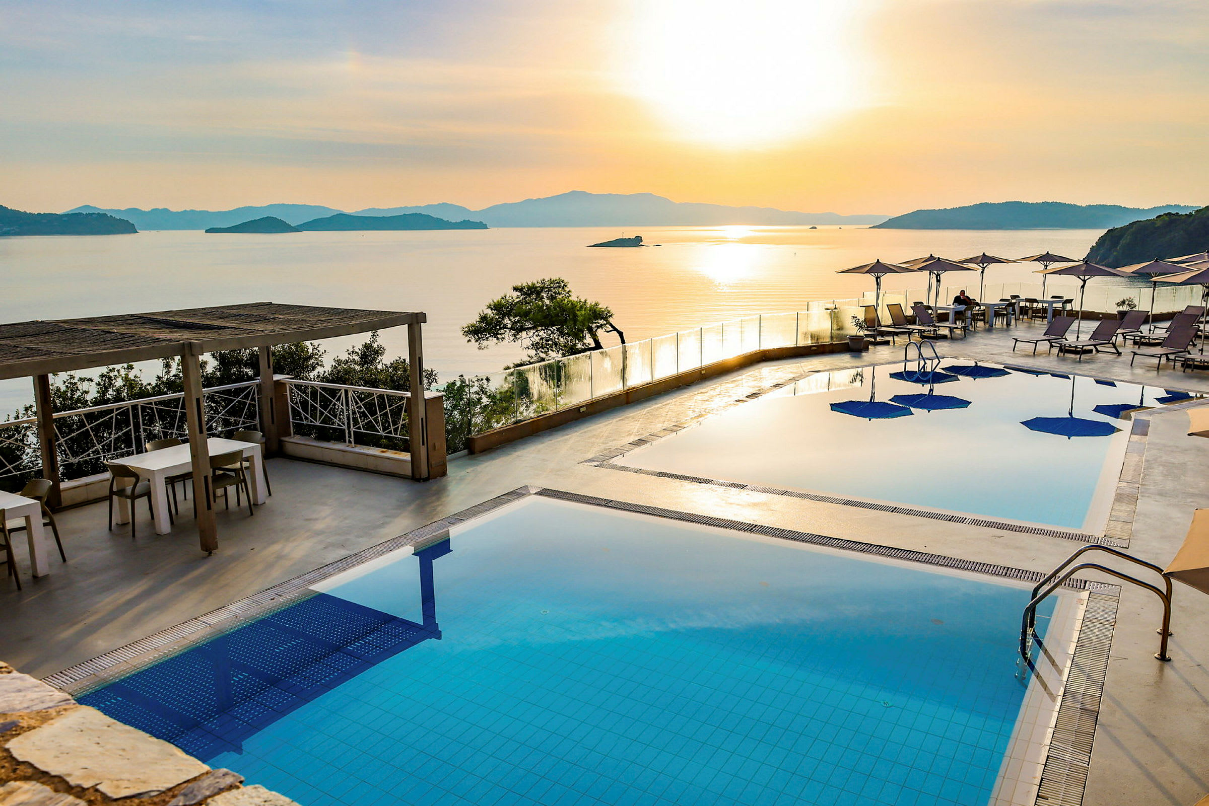 En poolterrasse med udsigt over havet og solnedgangen. (AI-genereret tekst)