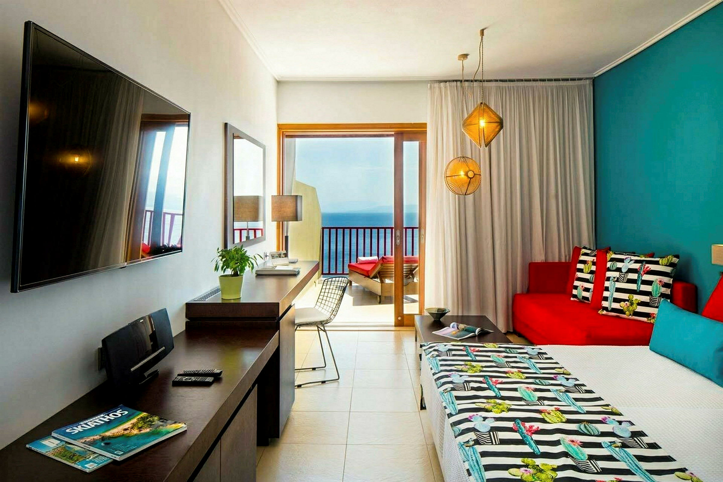 Et hotelværelse med farverigt interiør, en seng, sofa, bord og en altandør ud mod havet. (AI-genereret tekst)