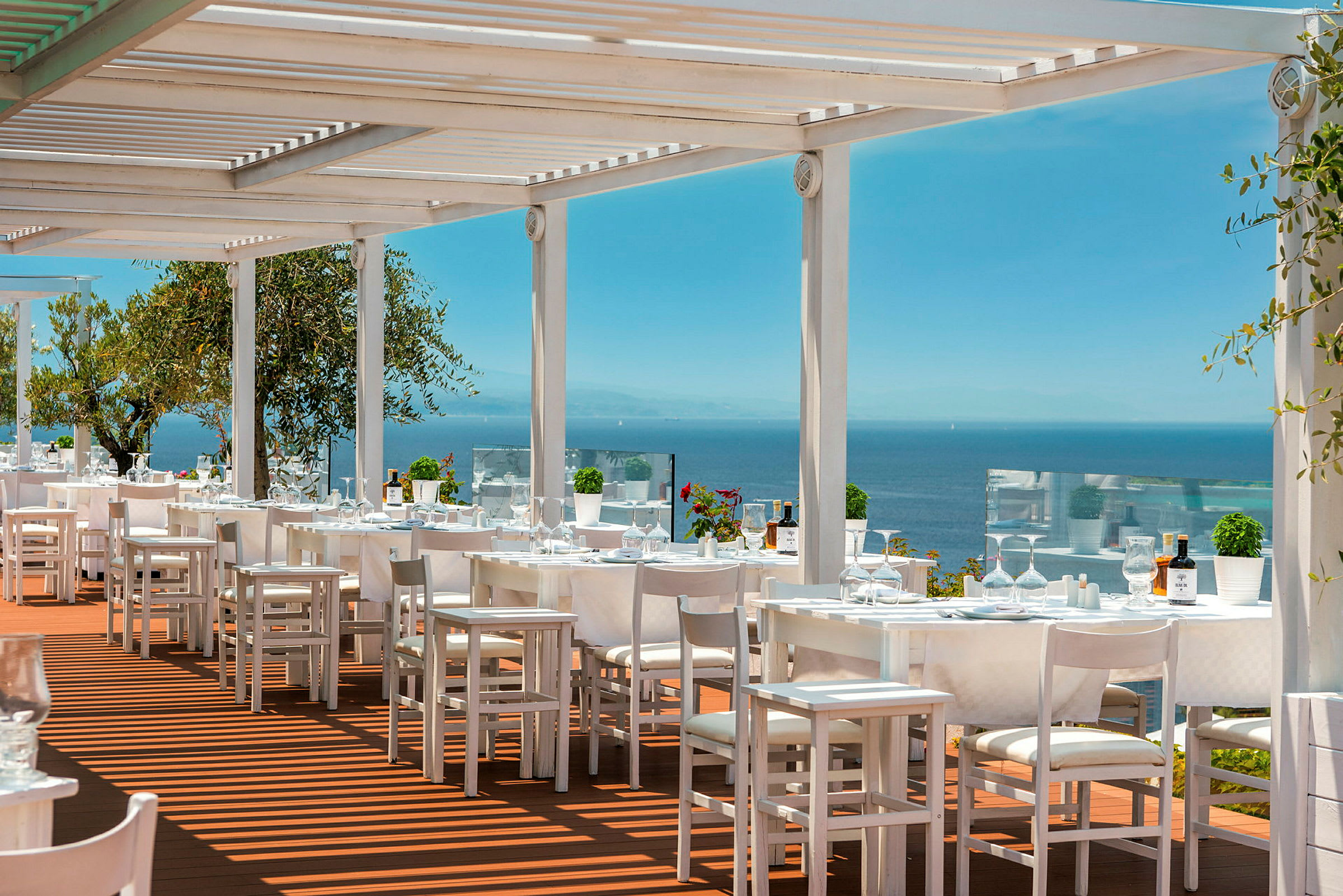 Udendørsrestaurant med hvide møbler og udsigt over havet. (AI-genereret tekst)