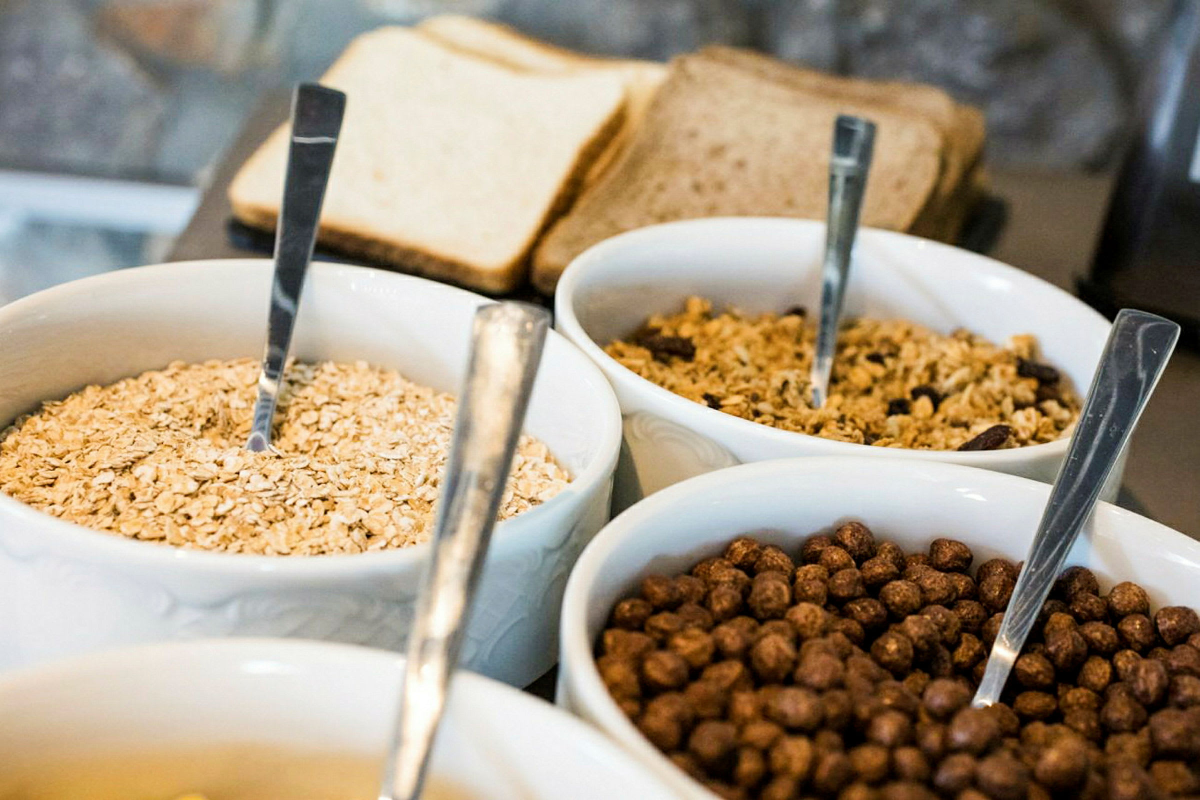 Skåle med forskellige typer morgenmadsprodukter og brød i baggrunden. (AI-genereret tekst)