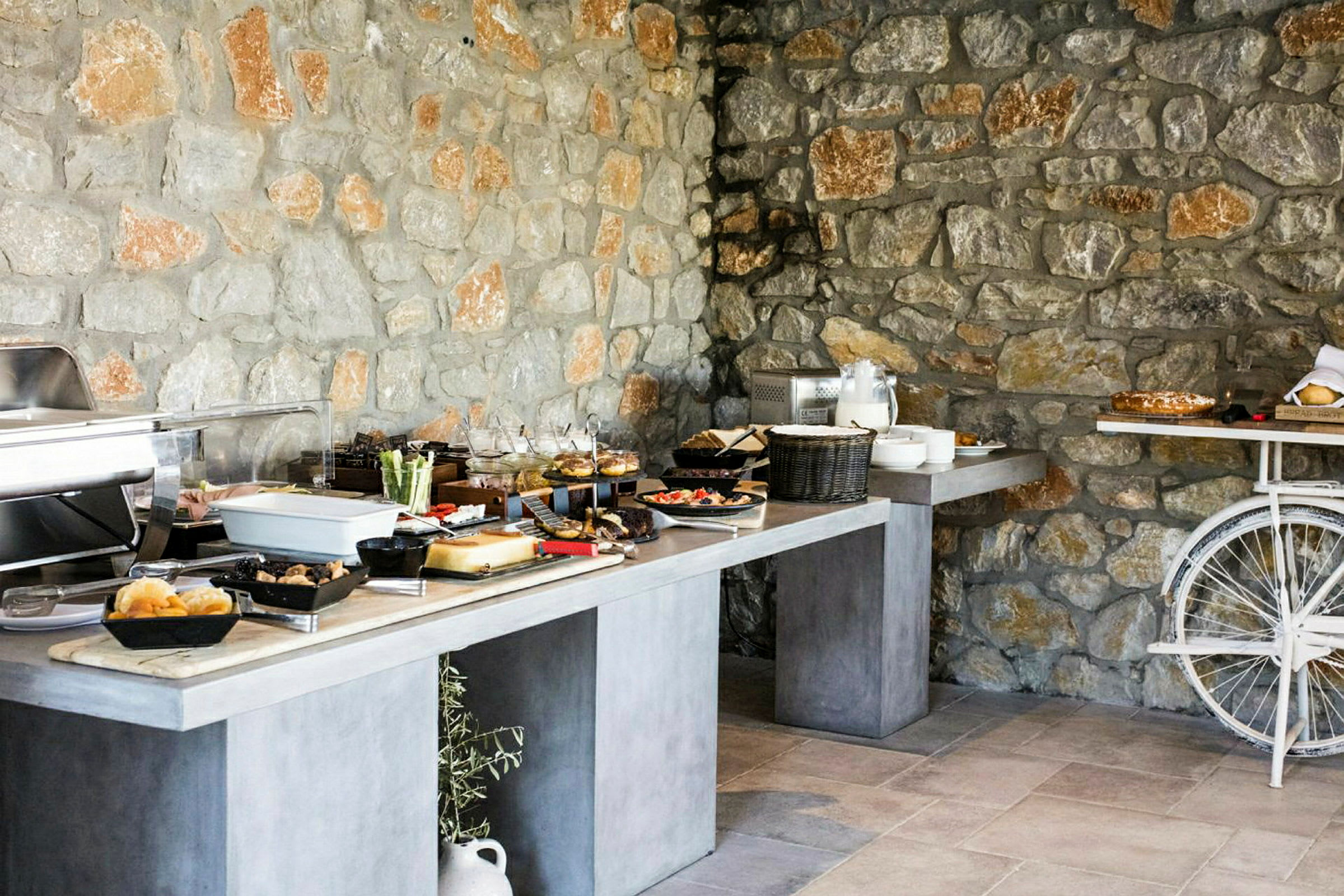 Buffetbord med forskellige retter foran en muret stenmur. (AI-genereret tekst)
