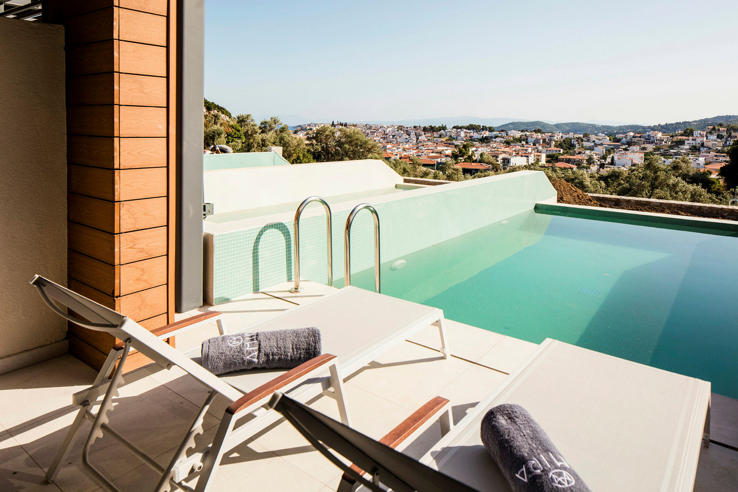 Terrasse med liggestole og en pool med udsigt over en by. (AI-genereret tekst)
