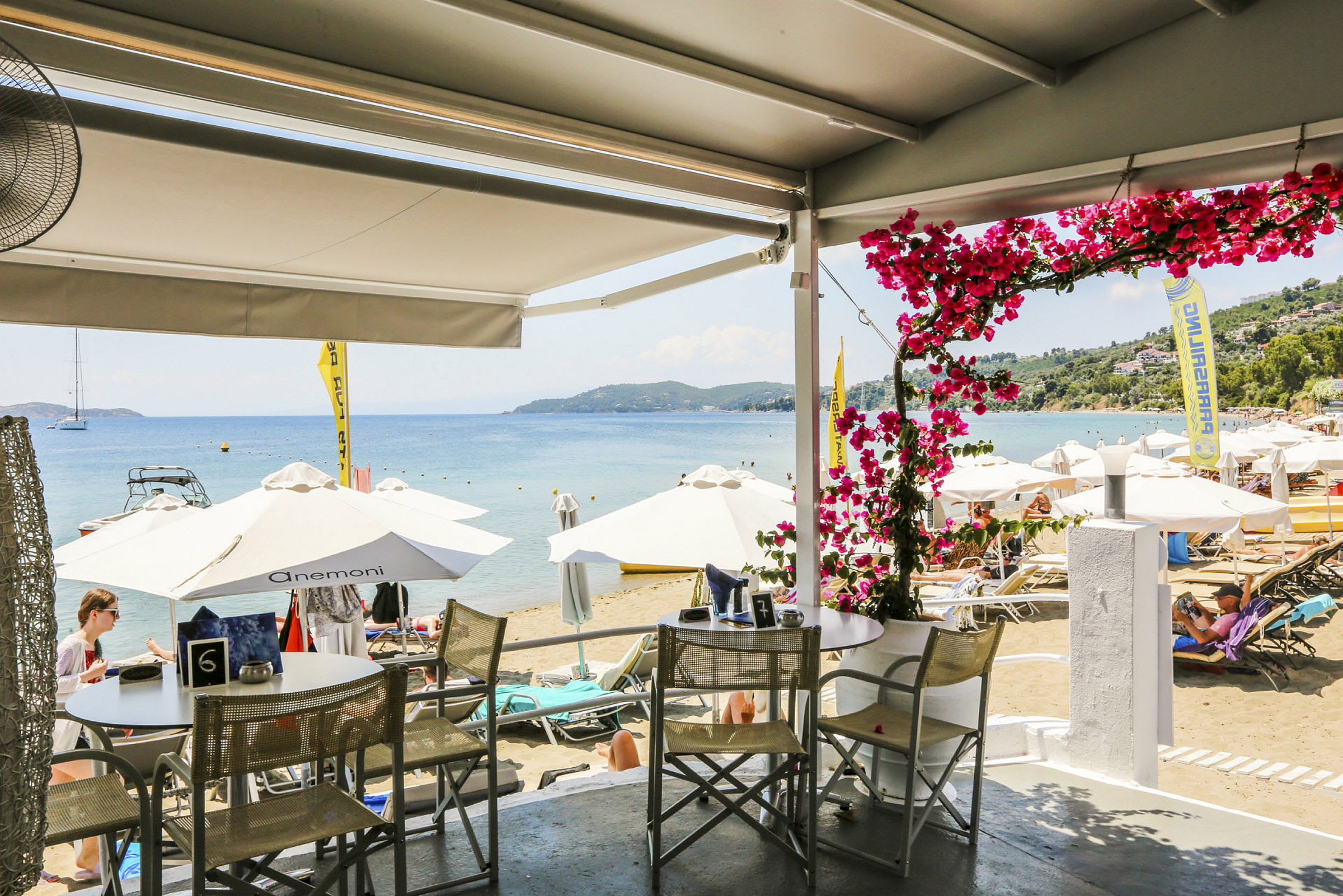 Udsigt fra en restaurant til en strand med parasoller og liggestole ved havet. (AI-genereret tekst)
