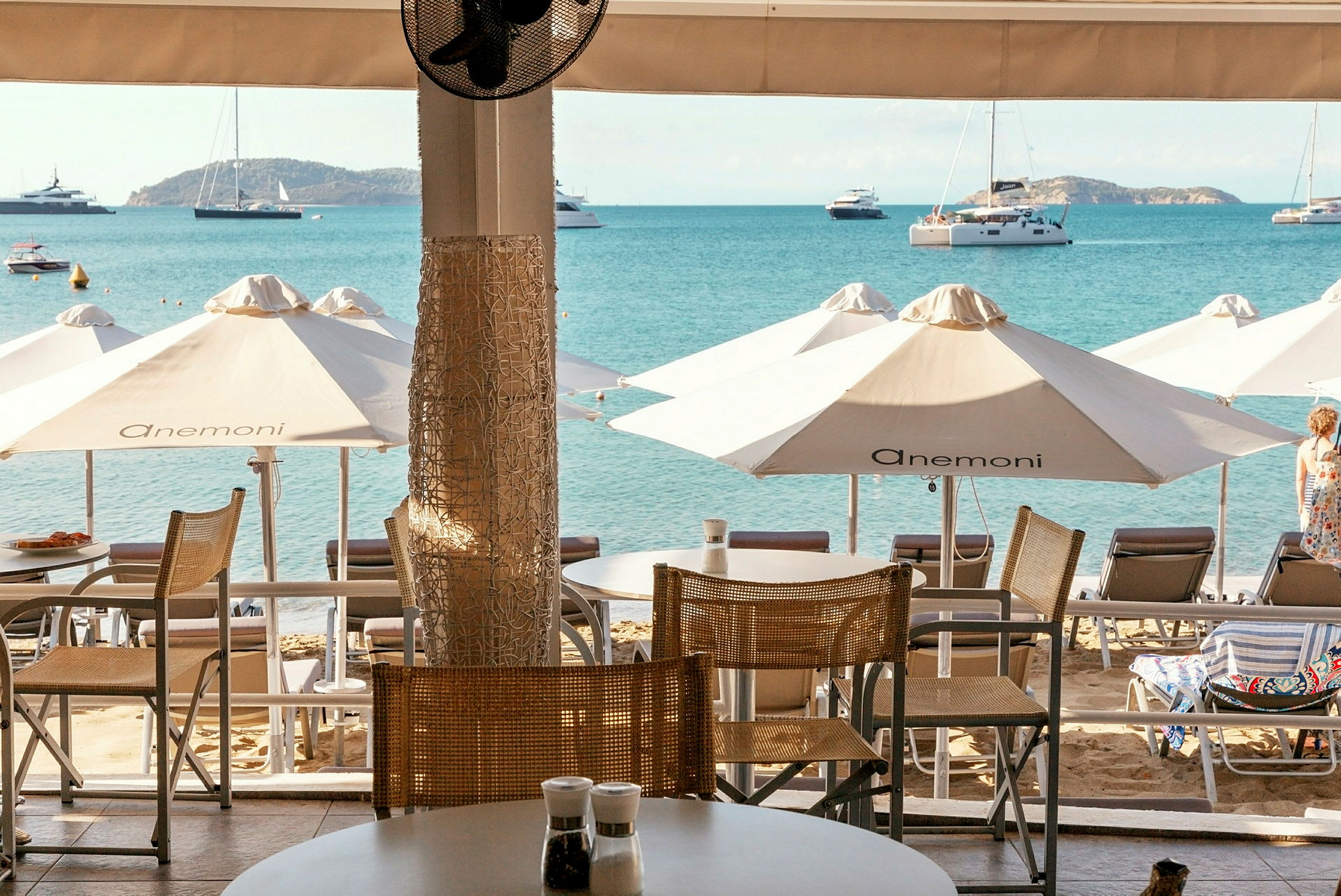 Udsigt fra en terrasse mod stranden med liggestole, parasoller og havet i baggrunden. (AI-genereret tekst)