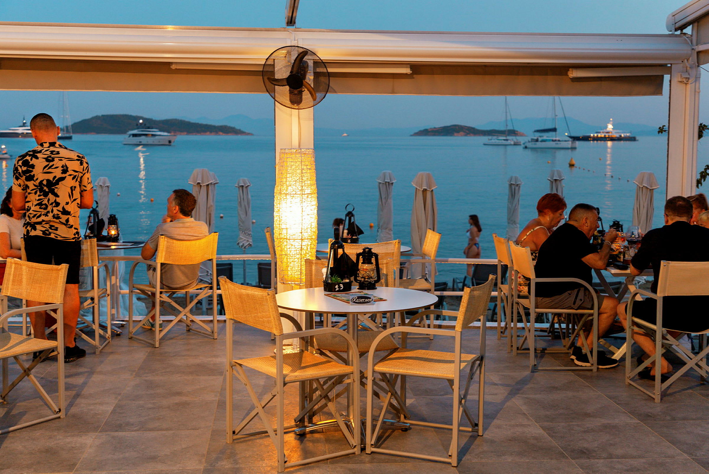 En restaurant med udsigt over havet og både ved solnedgang. (AI-genereret tekst)