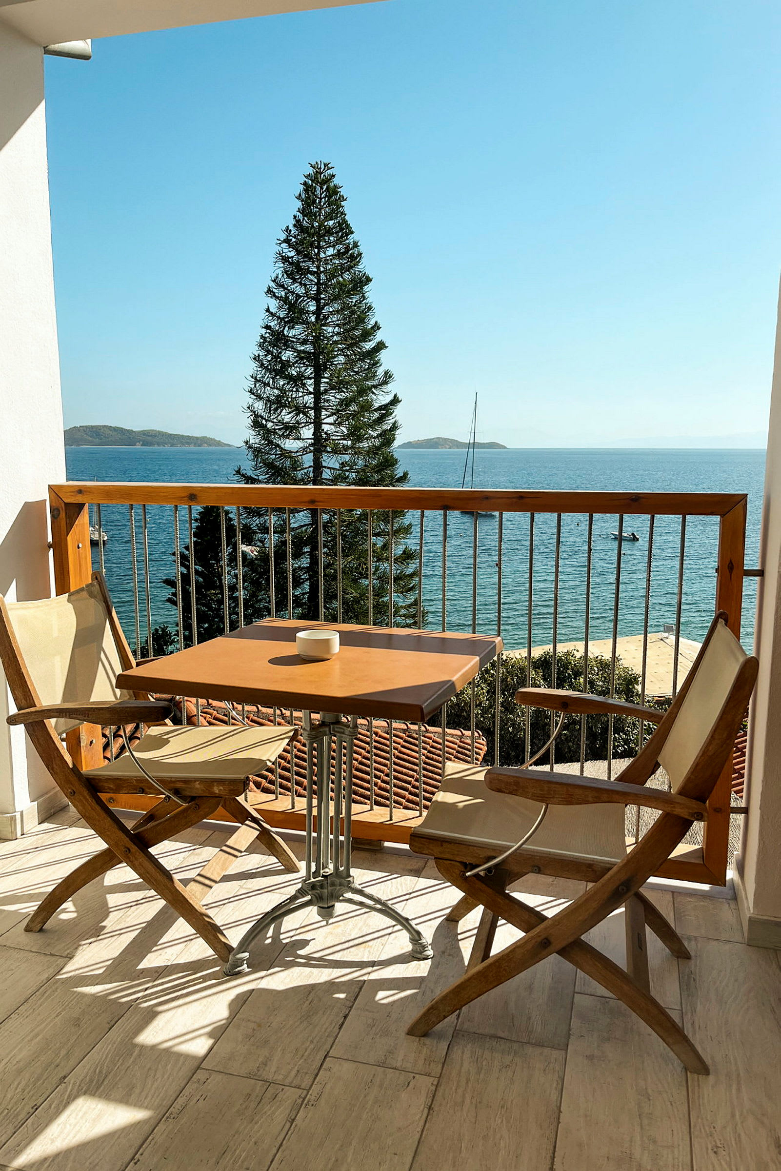 En balkon med to stole og et bord, havet og en mast er synlige i baggrunden. (AI-genereret tekst)