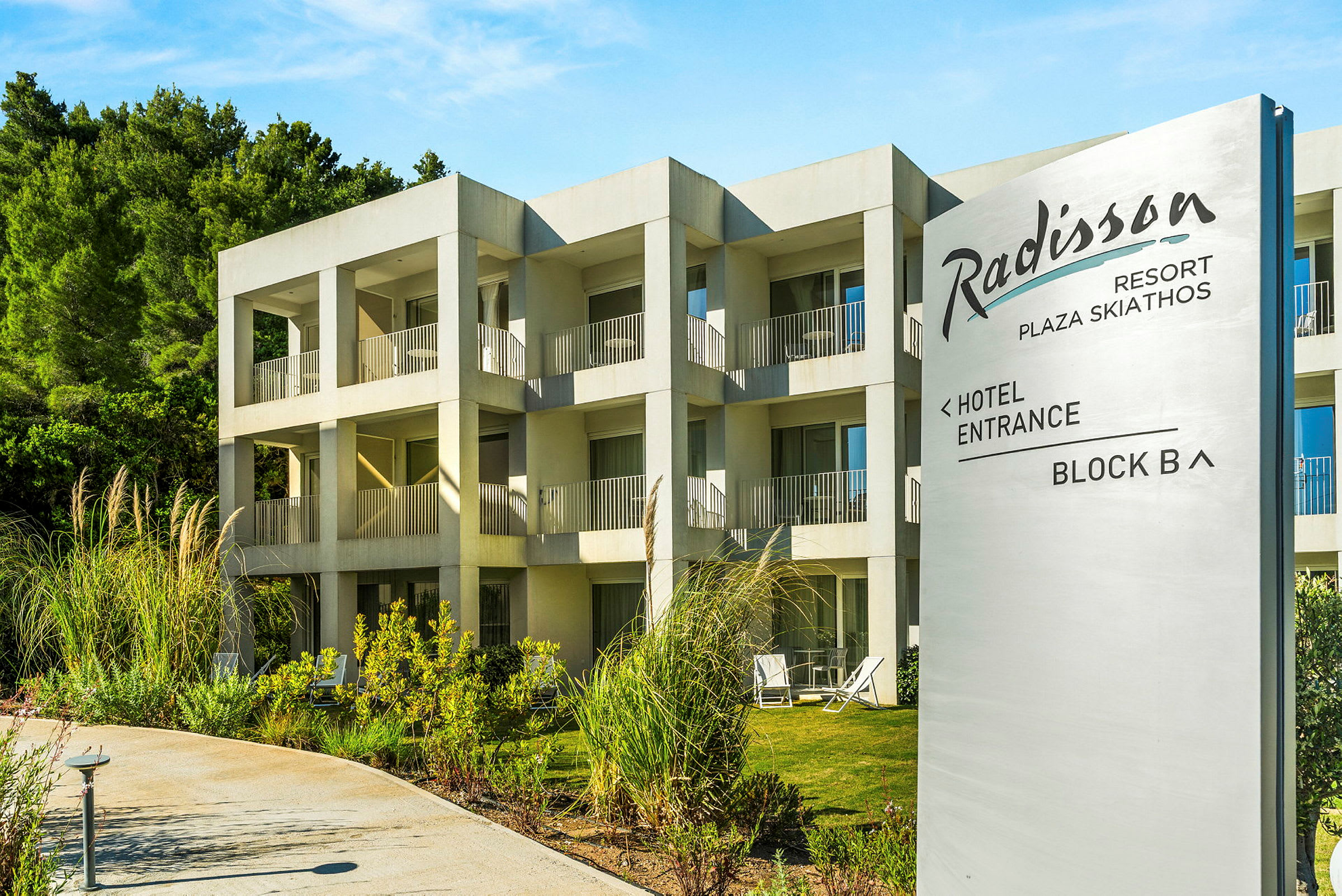Hotelbygning med flere værelser og altaner, med et skilt der viser Radisson Resort Plaza Skiathos. (AI-genereret tekst)