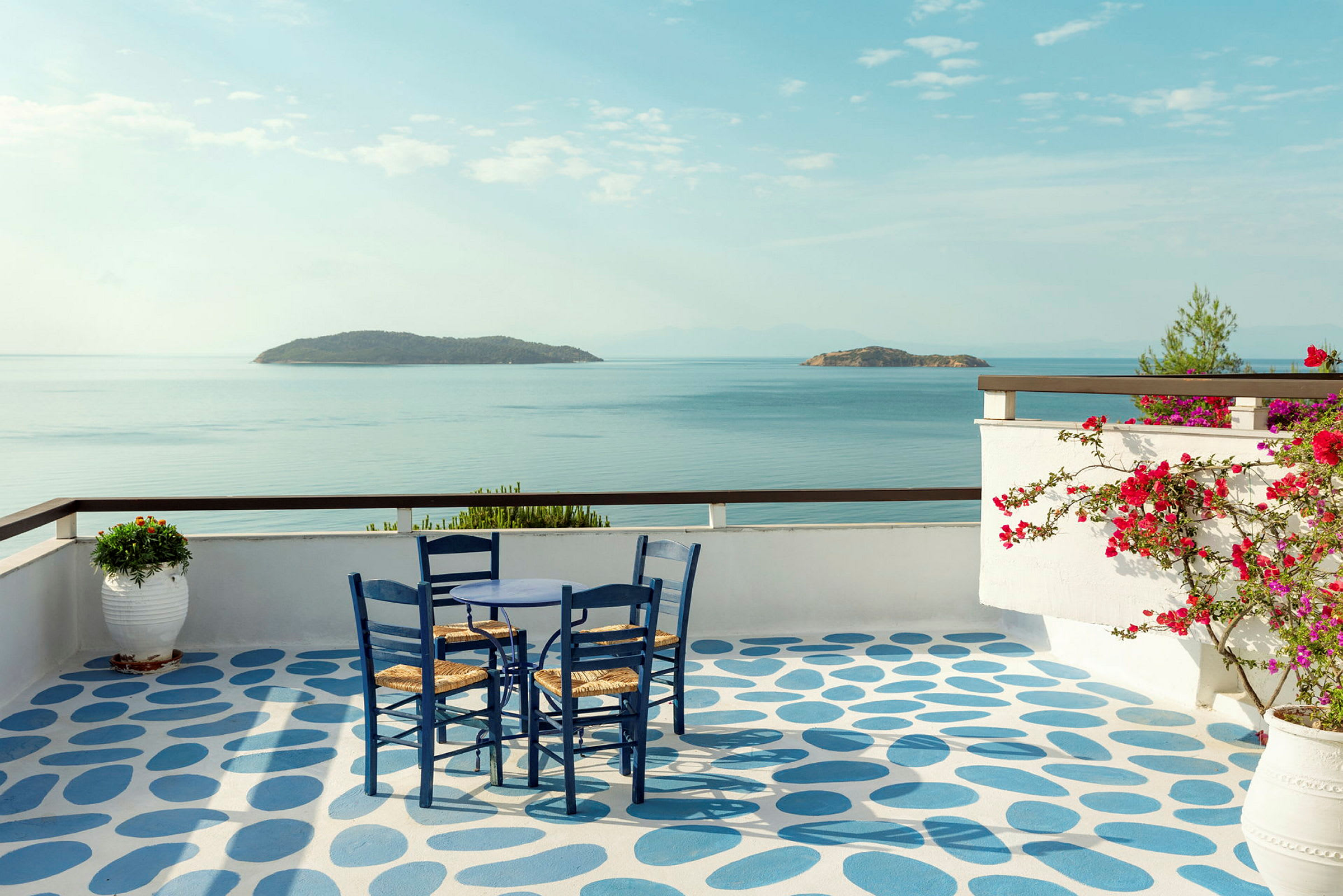 Udsigt over havet fra en terrasse med et bord og stole. (AI-genereret tekst)