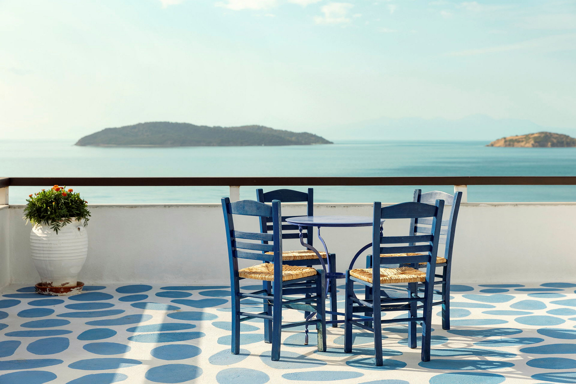 En blåmalet terrasse med bord og stole samt udsigt over havet og øer. (AI-genereret tekst)
