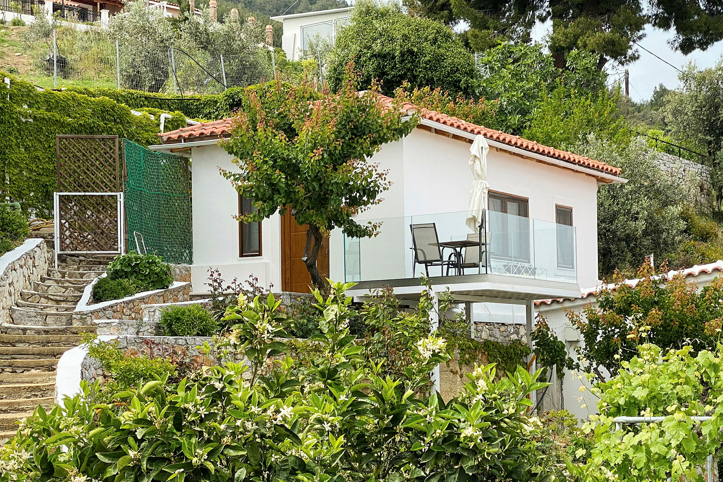 Hvidt hus med altan, omgivet af have og grønt. (AI-genereret tekst)