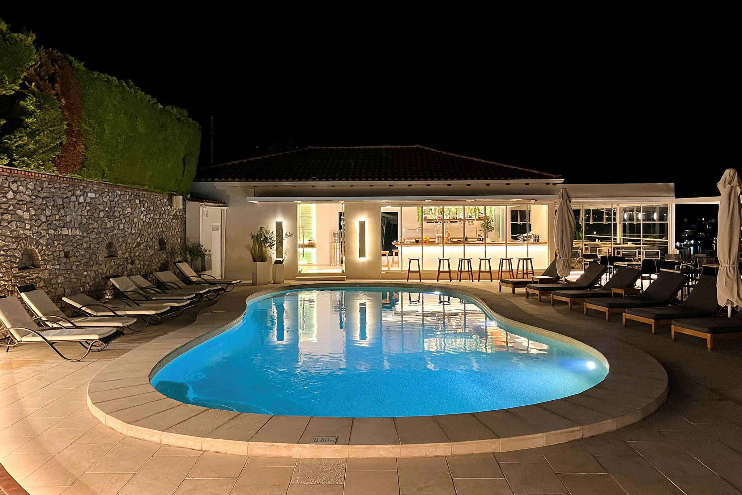 En oplyst udendørs swimmingpool ved en bar, der er åben om aftenen. (AI-genereret tekst)