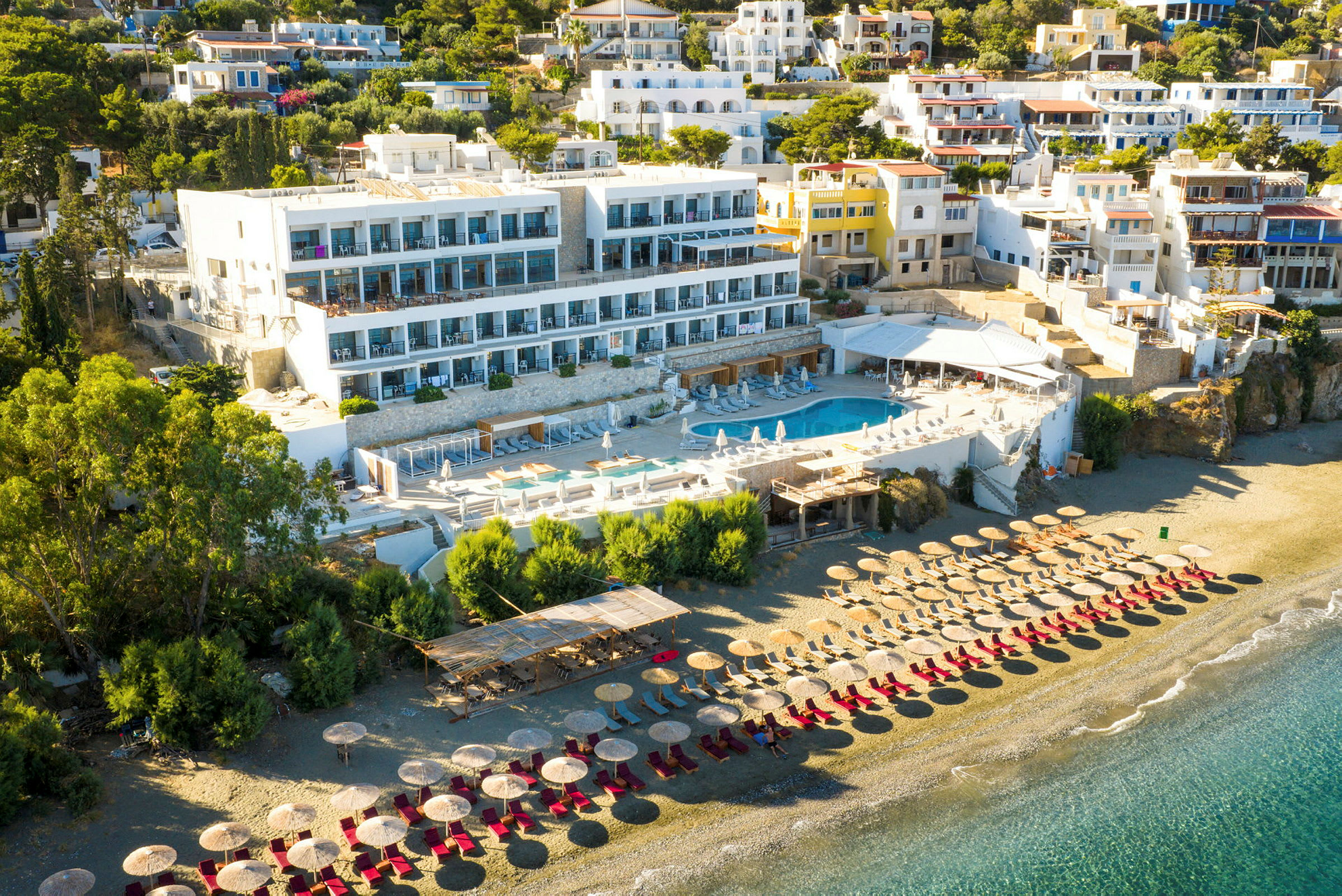 Hotelkompleks med poolområde og liggestole på en sandstrand. (AI-genereret tekst)