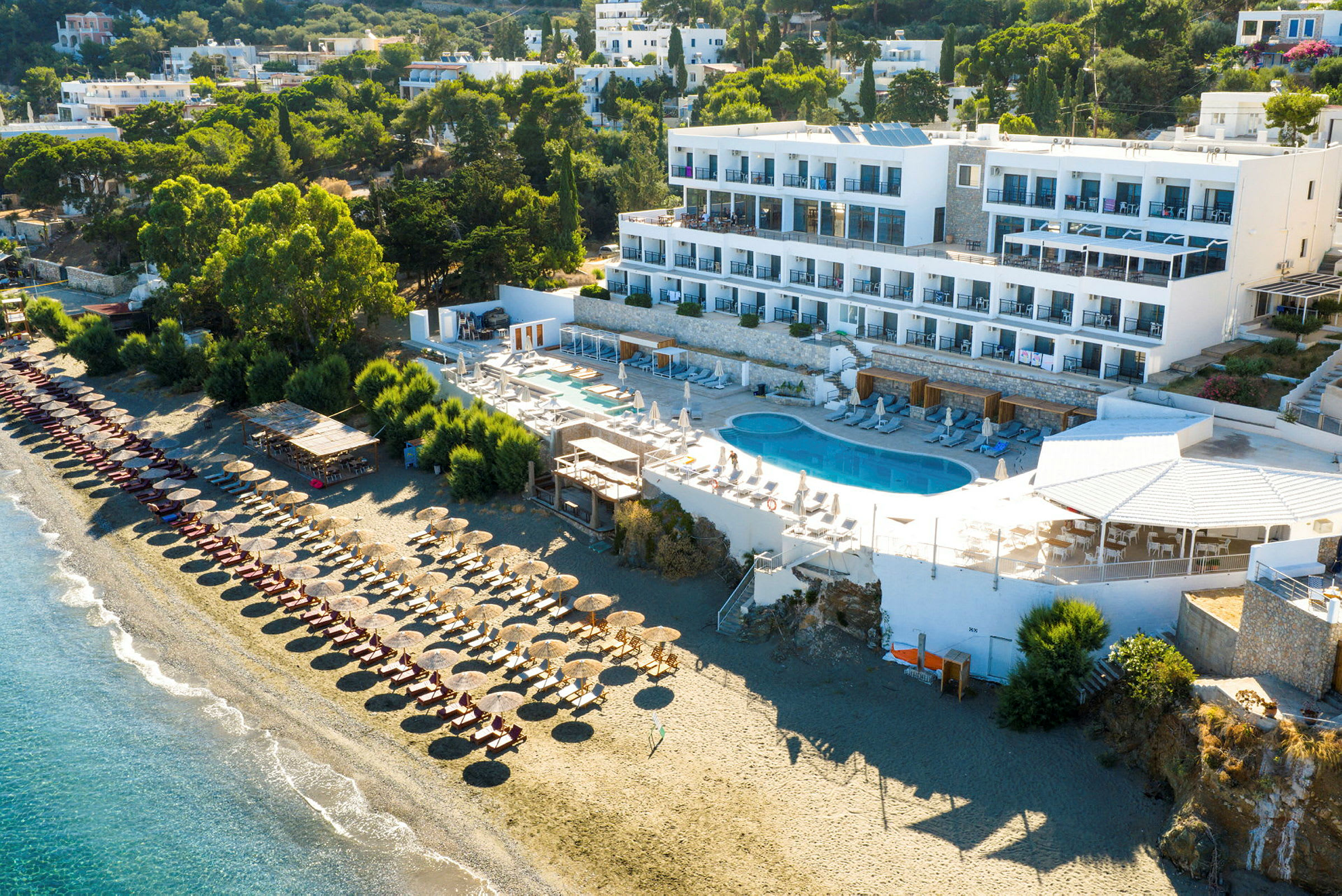 Udsigt over hotel ved stranden med pool og liggestole. (AI-genereret tekst)