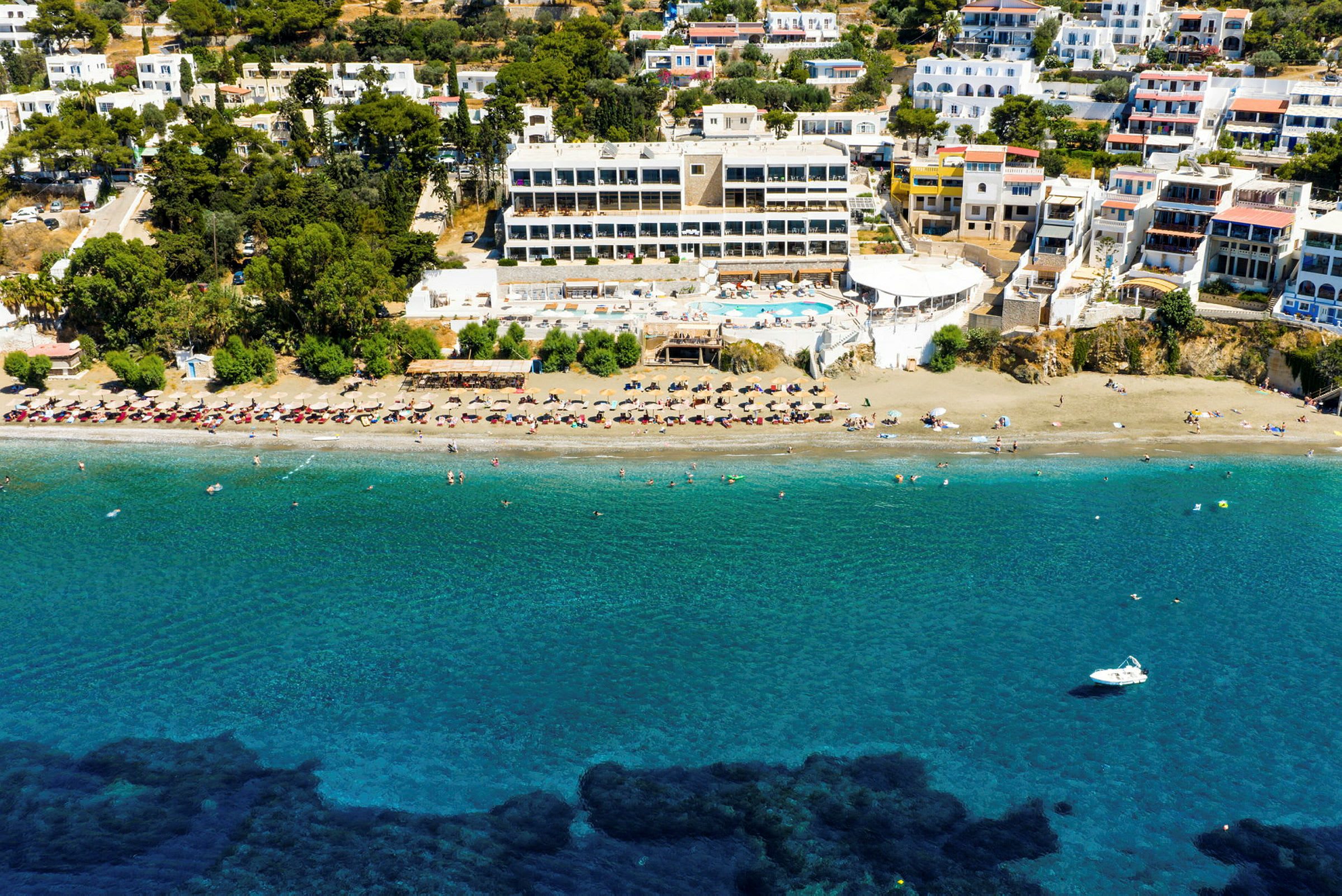 Billede af et hotelkompleks med swimmingpool tæt på en strand med liggestole og parasoller. (AI-genereret tekst)