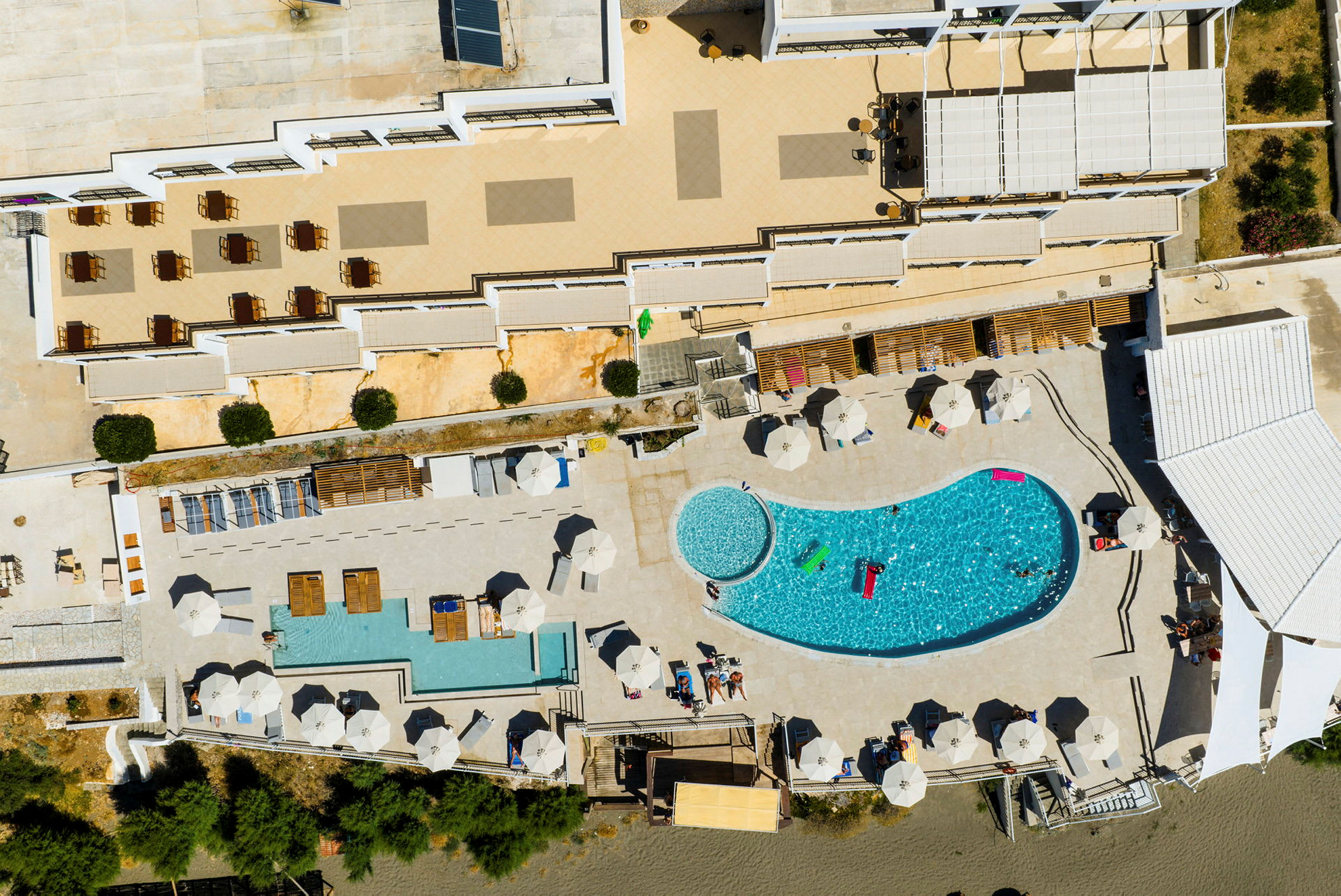 Luftfoto af et hotelområde med en pool, liggestole og parasoller. (AI-genereret tekst)