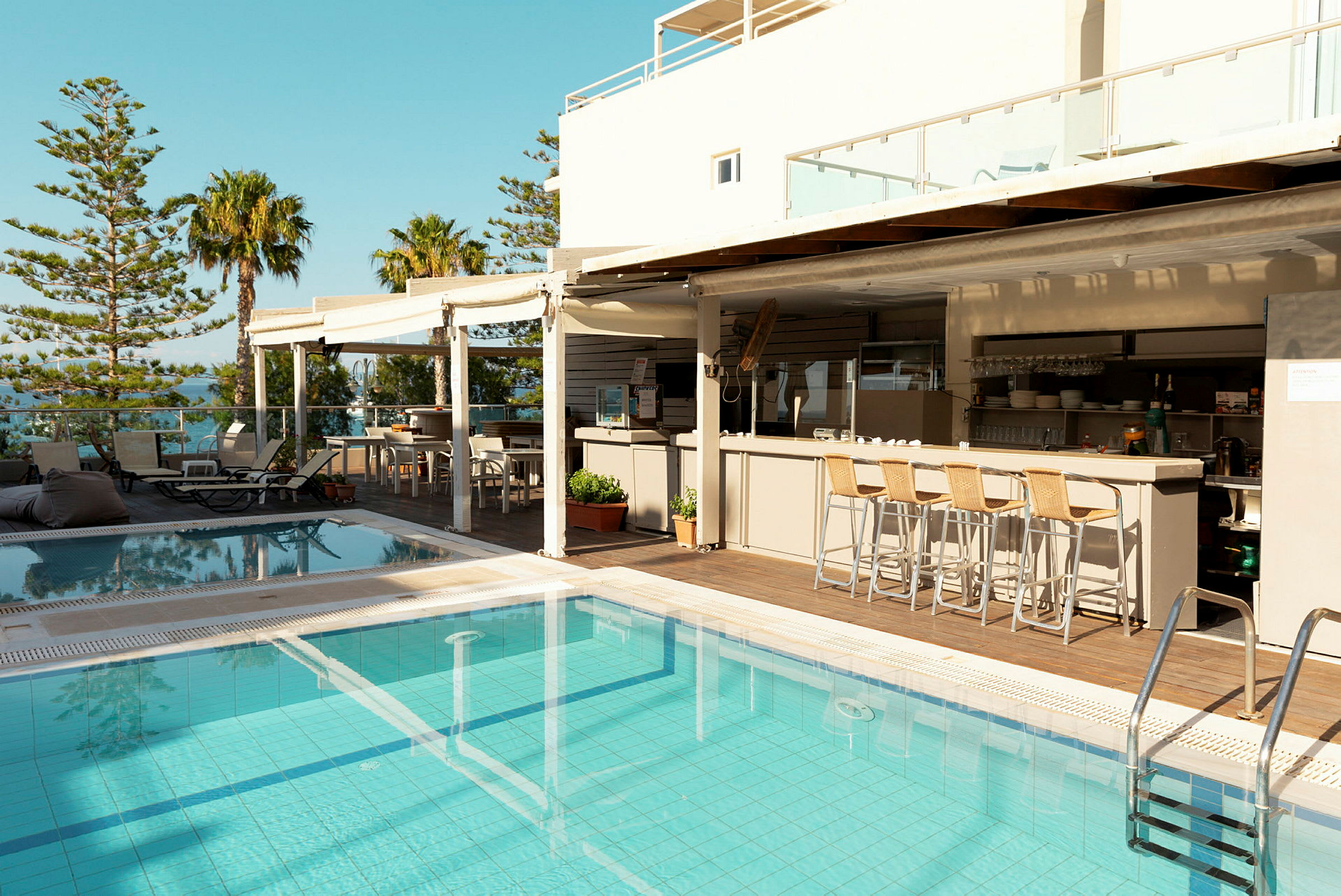 Udendørs pool nær en bar og spiseområde, omgivet af træer og himmel. (AI-genereret tekst)