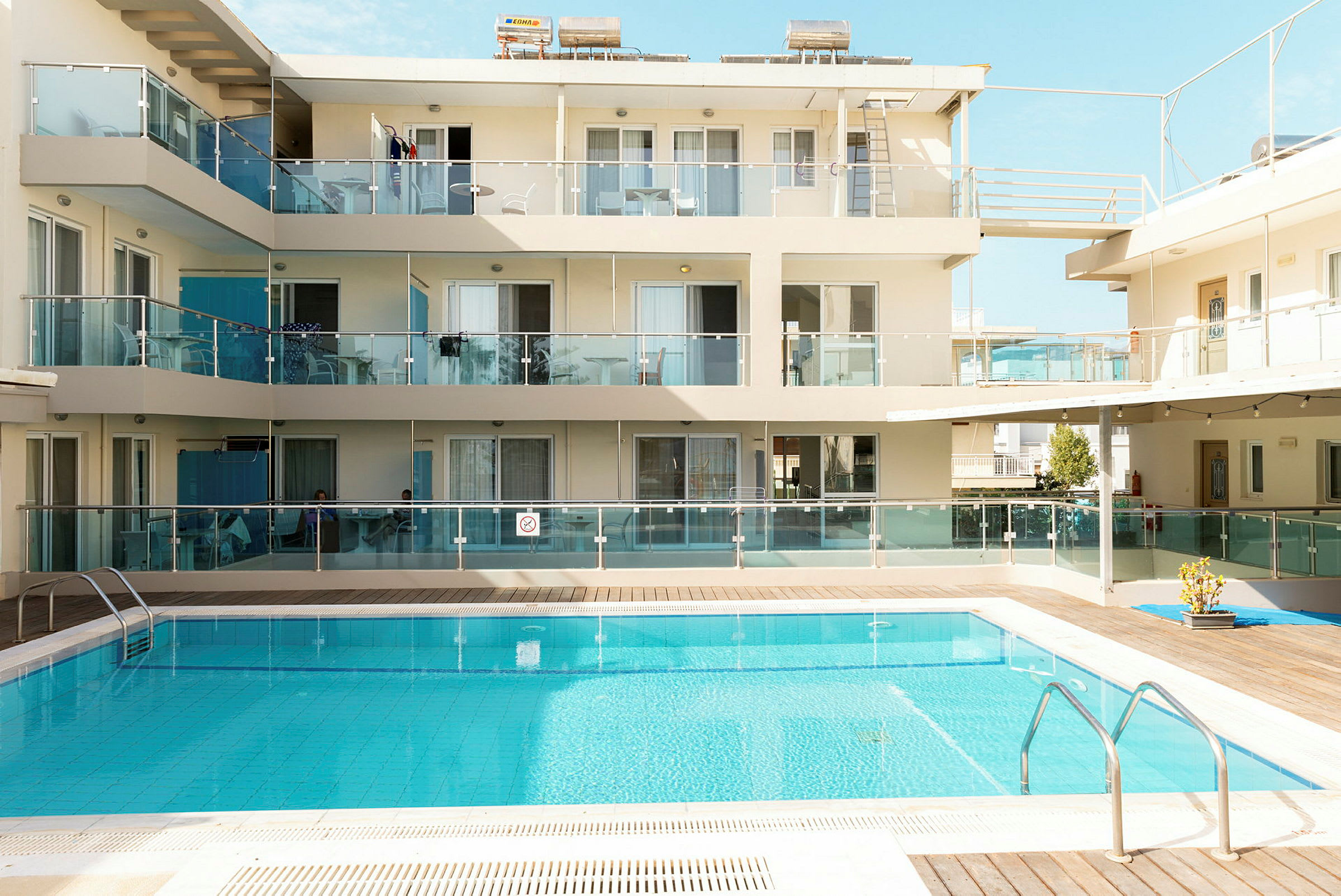 Billedet viser et hotel med altaner og en udendørs swimmingpool. (AI-genereret tekst)