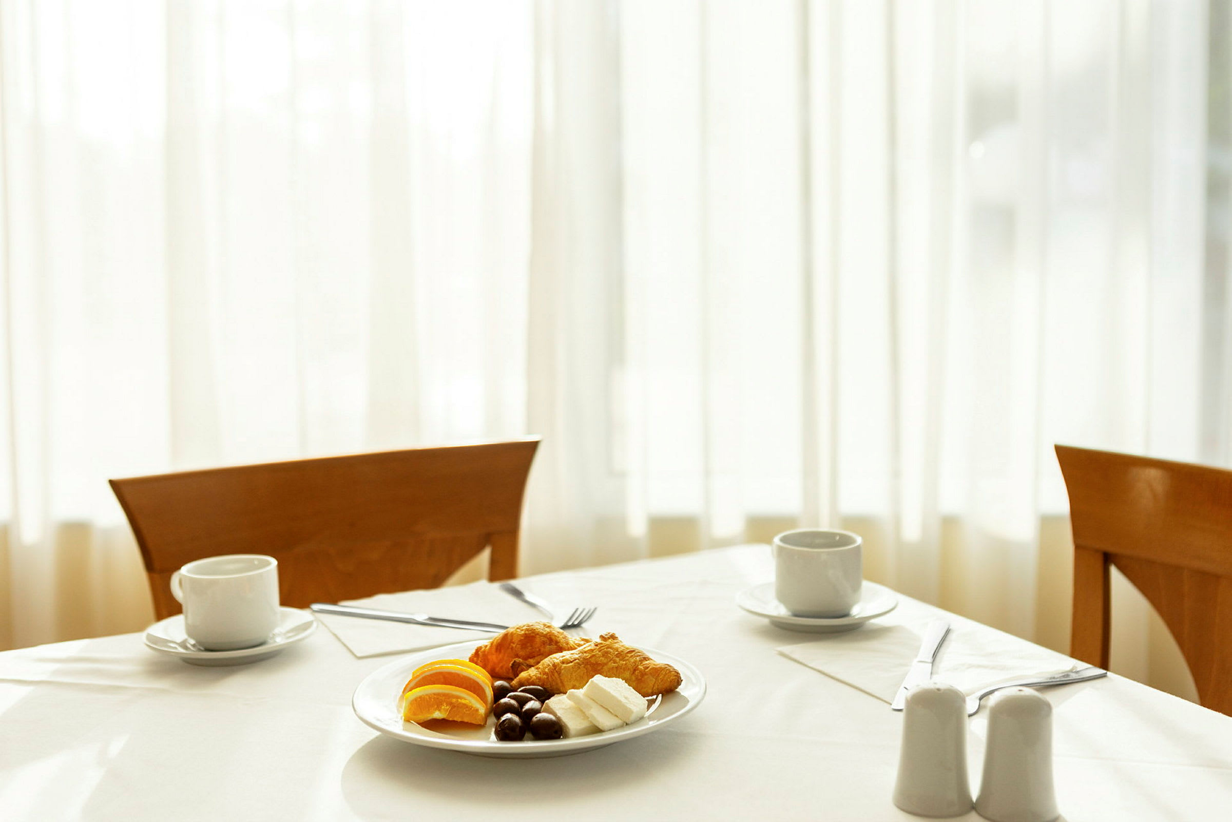 En dækket morgenmad med en tallerken indeholdende croissanter, appelsinskiver, ost og chokolade samt to kopper kaffe. (AI-genereret tekst)
