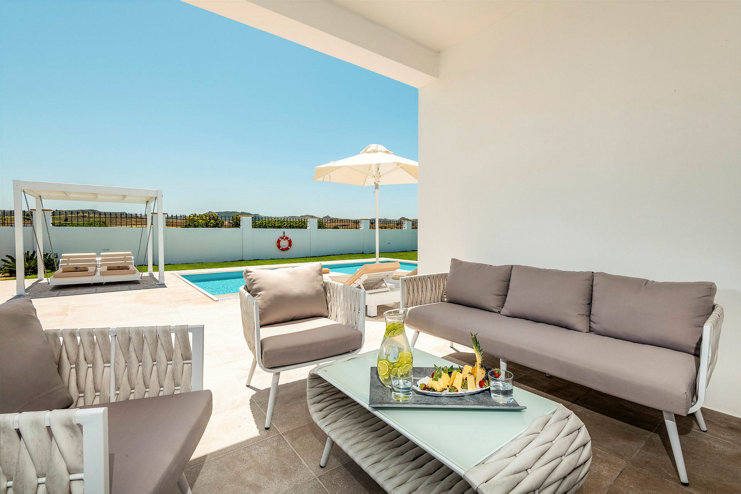 Billede af en terrasse med udendørsmøbler, en pool og en pergola i baggrunden. (AI-genereret tekst)