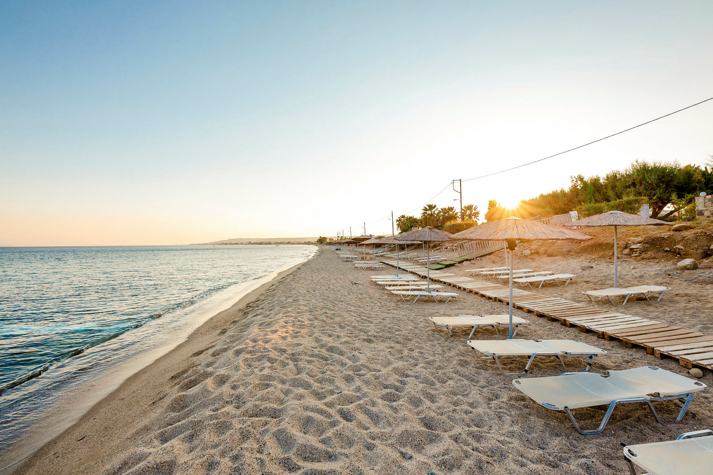 Strand med liggestole og parasoller ved solnedgang. (AI-genereret tekst)