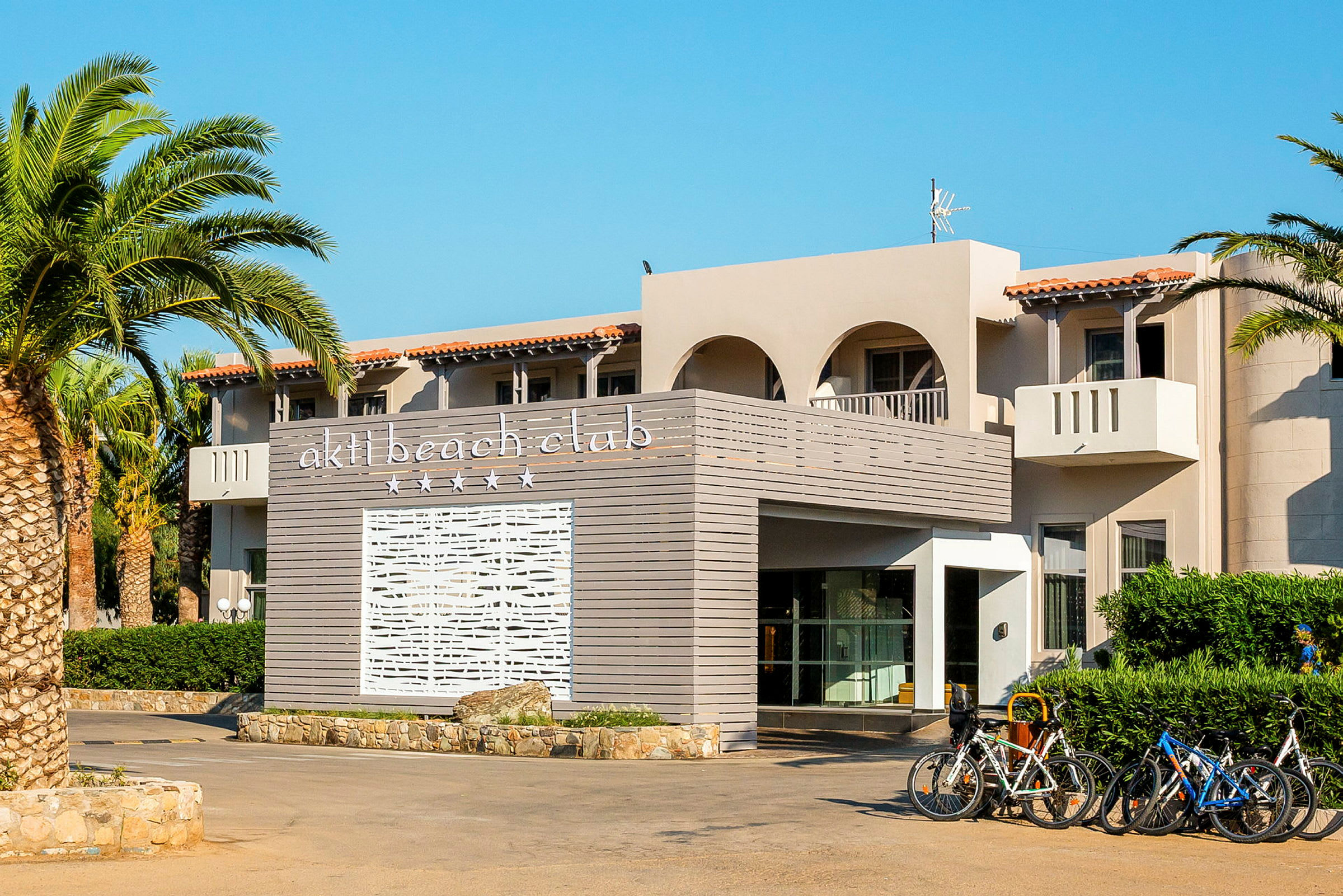 Bygning med teksten 'akti beach club' på en panel i forgrunden og cykler parkeret ved indgangen. (AI-genereret tekst)