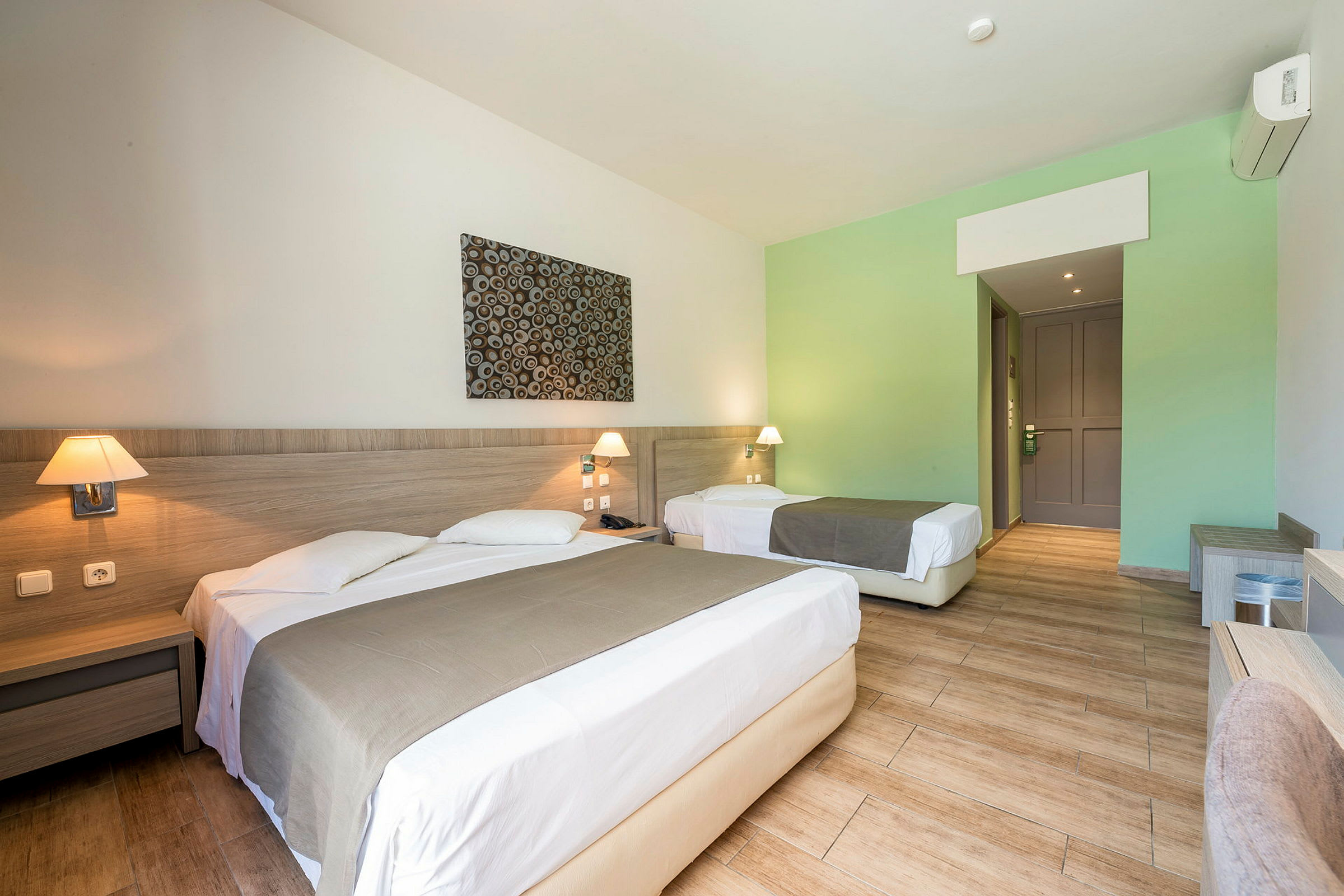 Hotelværelse med en dobbeltseng og en enkeltseng, begge med sengetæpper og natborde. (AI-genereret tekst)