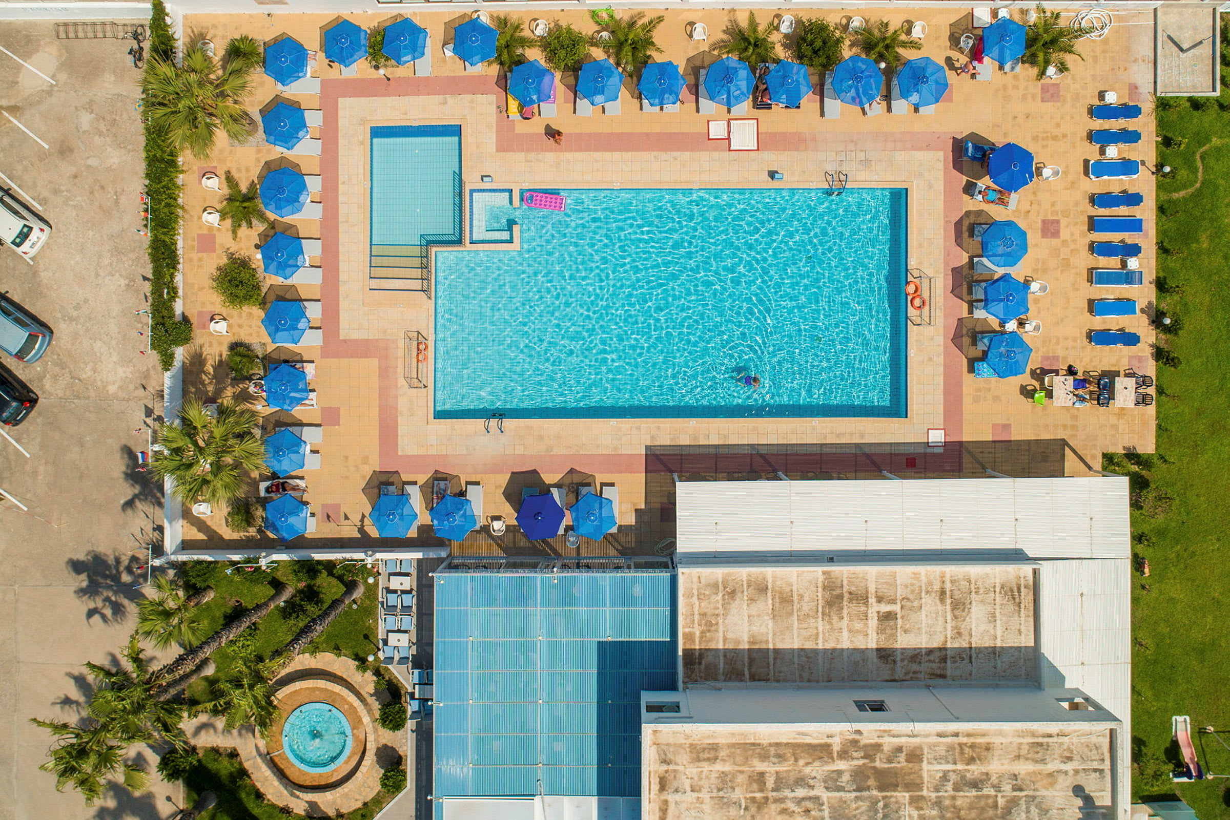 Luftfoto af et poolområde med liggestole og parasoller omkring poolen. (AI-genereret tekst)