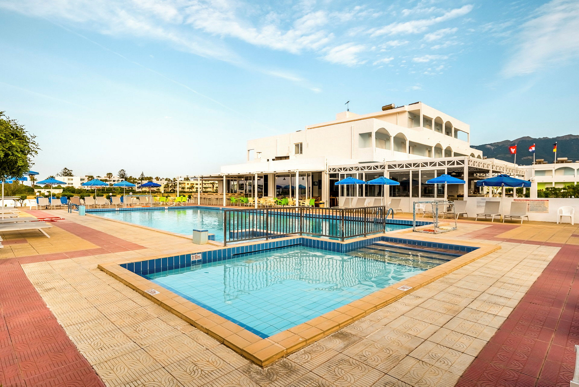 En udendørs swimmingpool omgivet af liggestole og parasoller ved et hotel. (AI-genereret tekst)