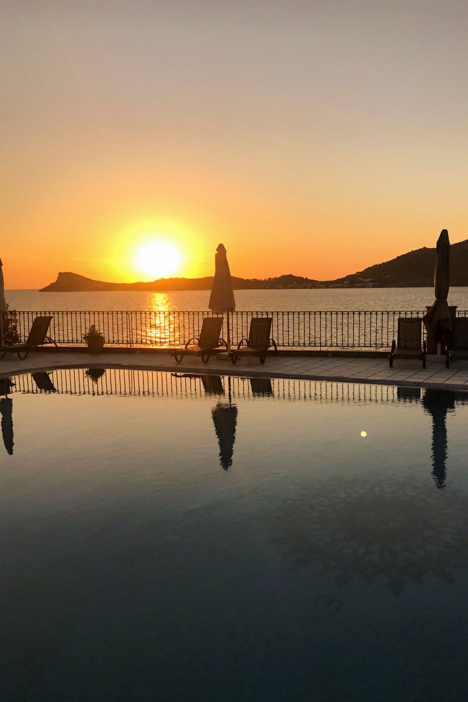 En solnedgang over havet med en pool og liggestole i forgrunden. (AI-genereret tekst)