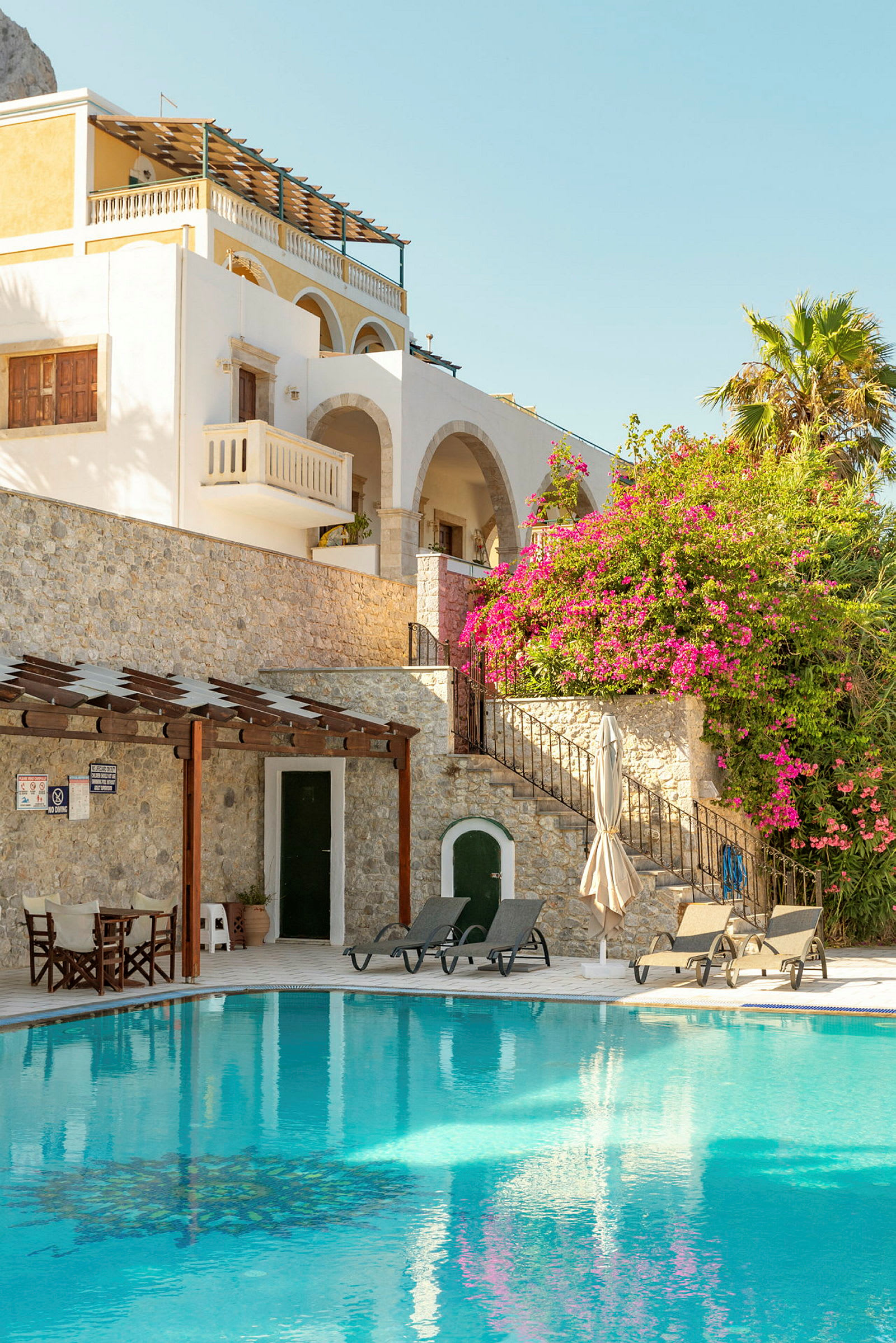 Billede af en pool foran en bygning med murstensfacade og bougainvillea. (AI-genereret tekst)