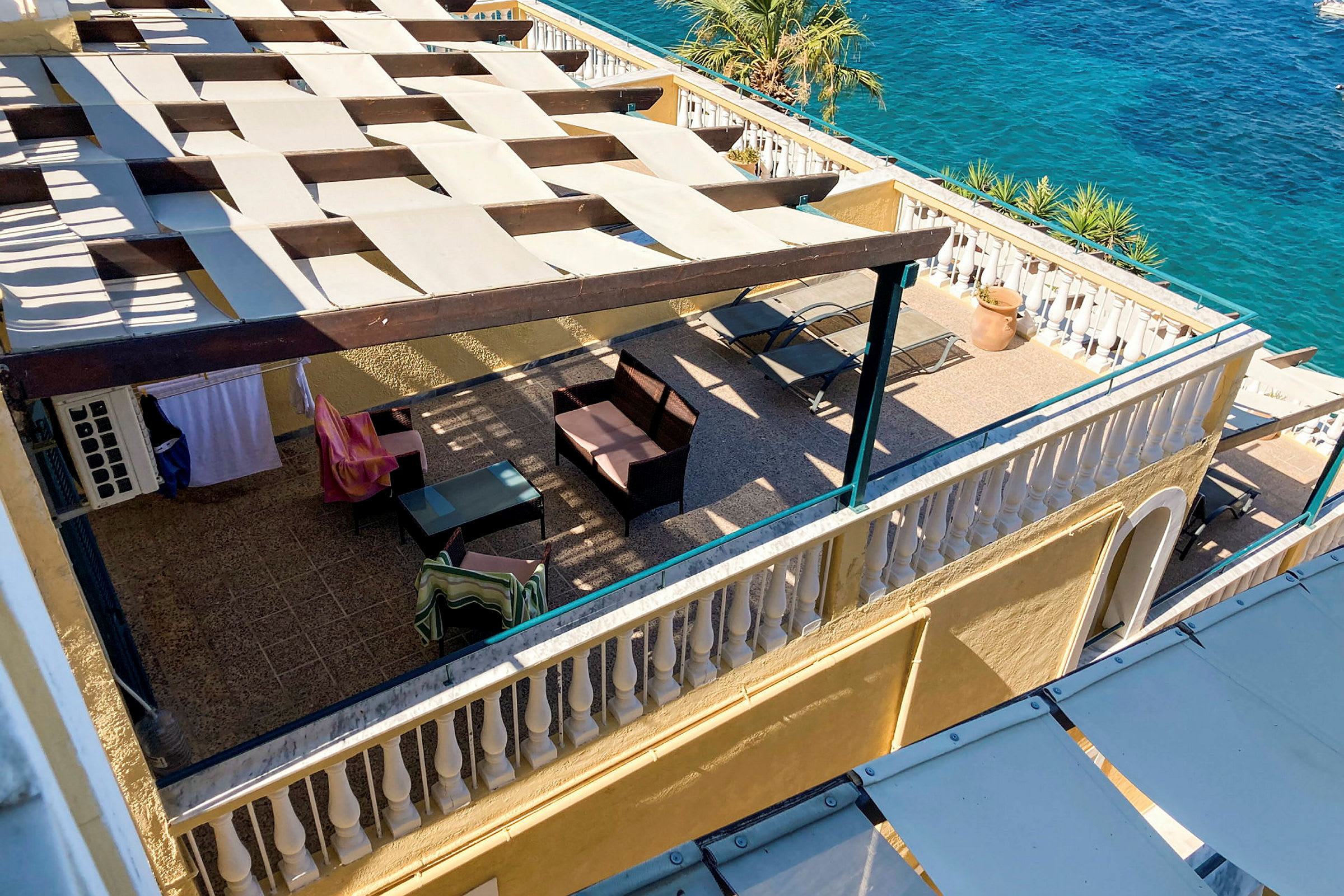 En udsigt over en terrasse med skyggefuld pergola, møbler og udsigt til havet. (AI-genereret tekst)