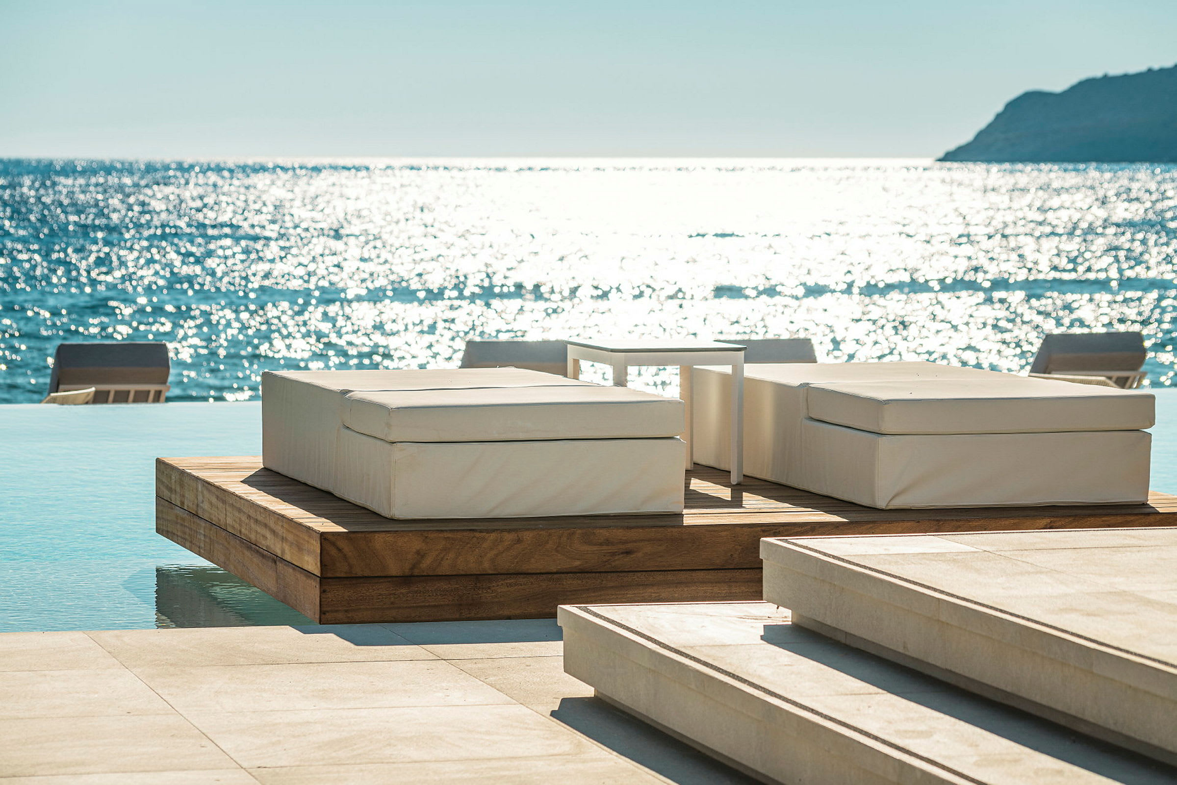 Liggestole ved en infinitypool med havet i baggrunden. (AI-genereret tekst)