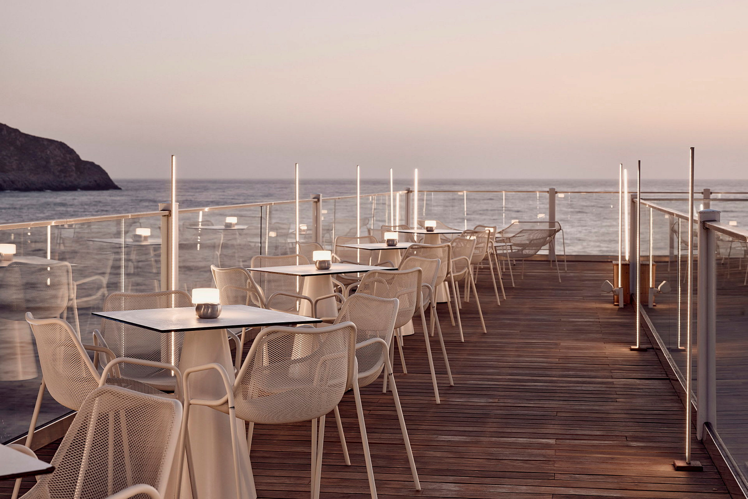 En terrasse med borde og stole ved havet og solnedgang. (AI-genereret tekst)