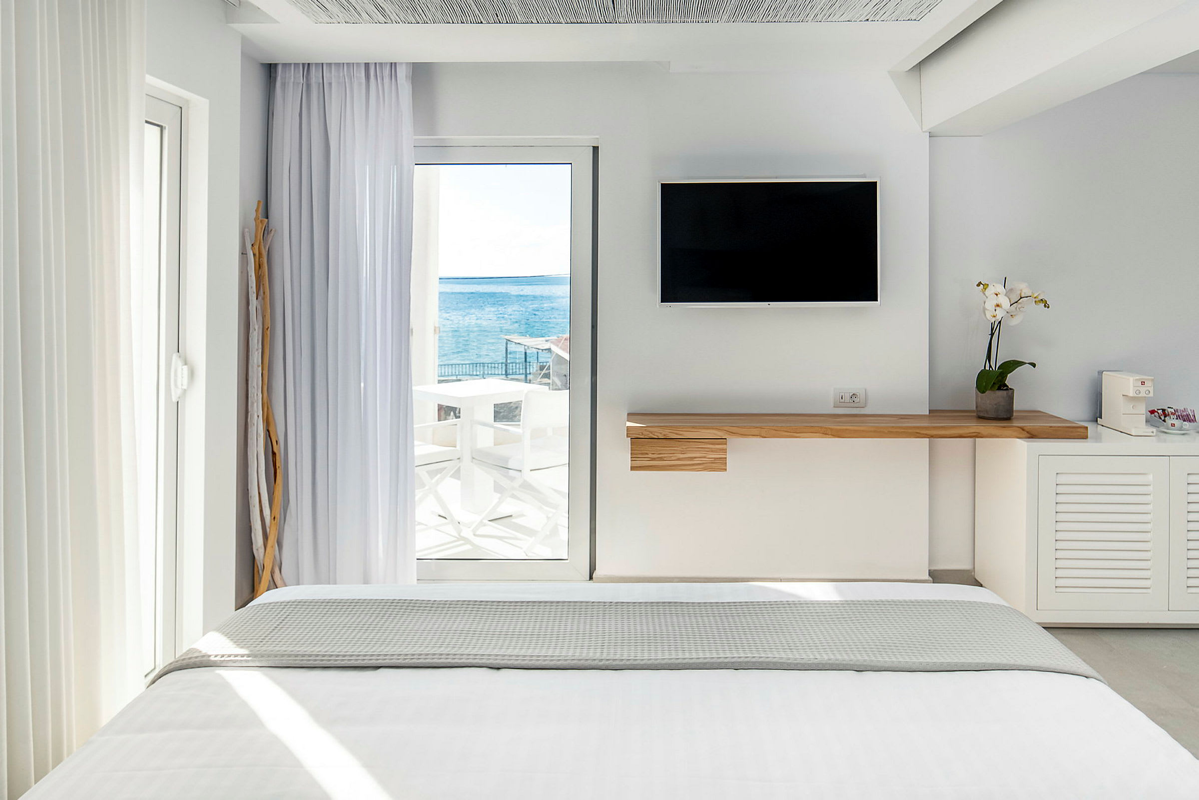 Interiør af et lyst hotelværelse med en seng og havudsigt gennem en glasdør. (AI-genereret tekst)