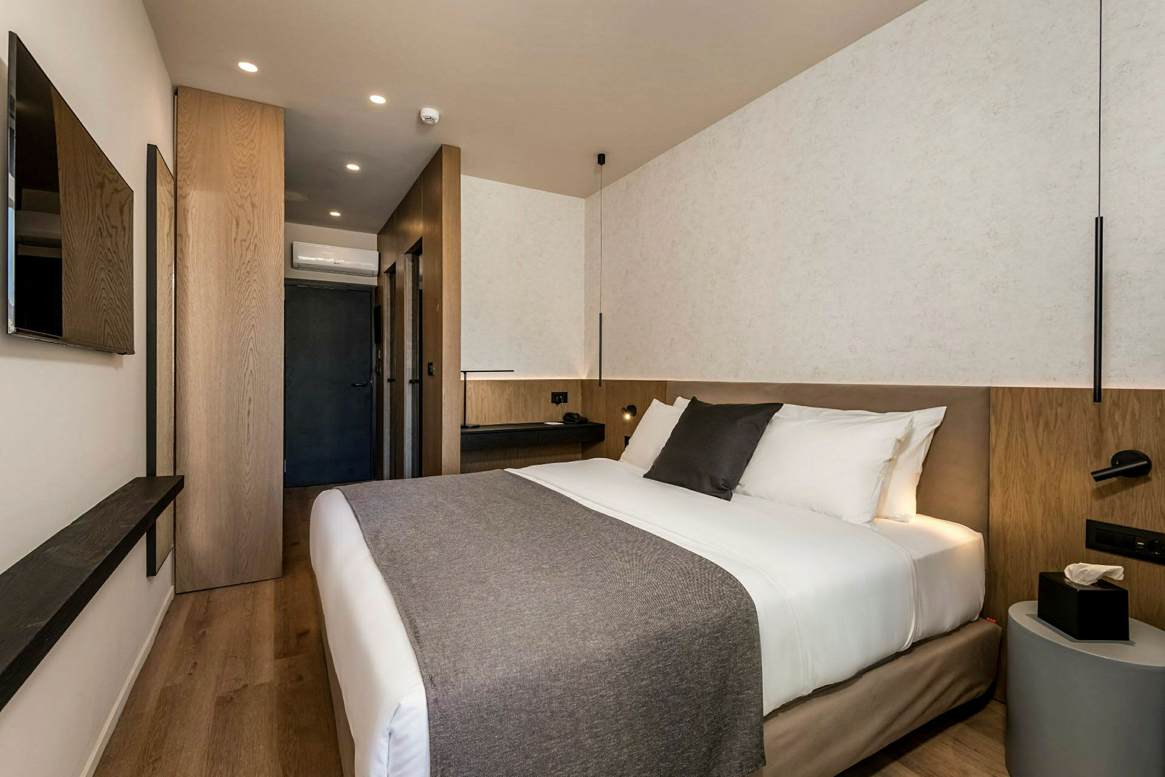 Moderne hotelværelse med dobbeltseng, natbord og vægmonteret TV. (AI-genereret tekst)