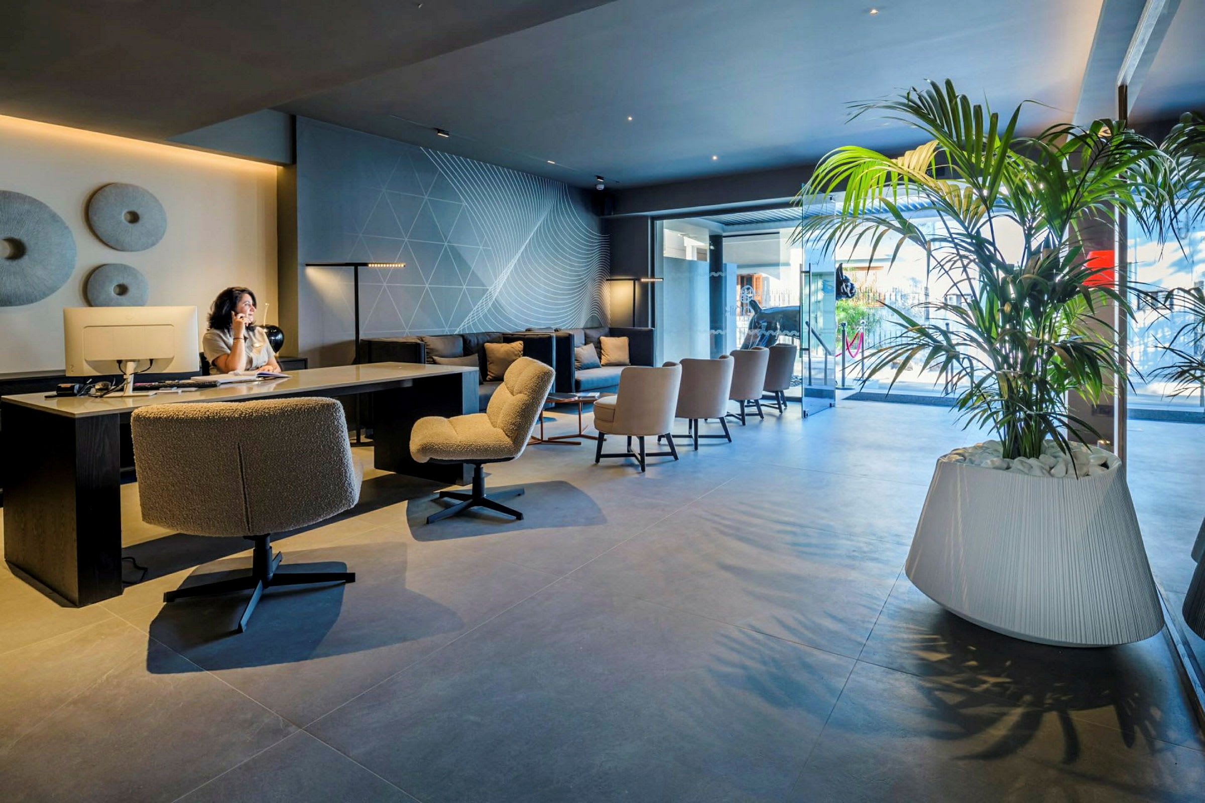 Interiør af en moderne lobby med siddepladser, skrivebord og store grønne planter. (AI-genereret tekst)