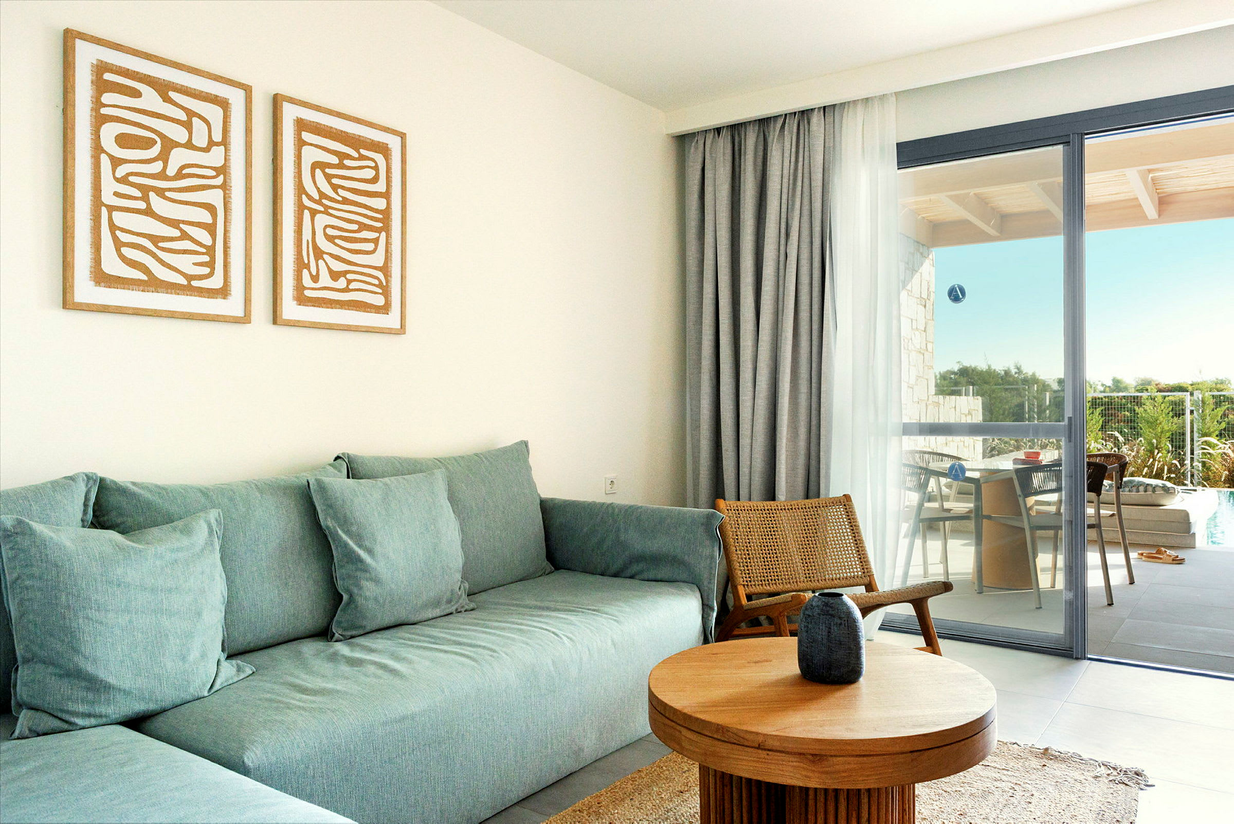 Stue med turkis sofa, træbord og en stol af flet. Vindue med gardin og udsigt til balkon med siddepladser. (AI-genereret tekst)
