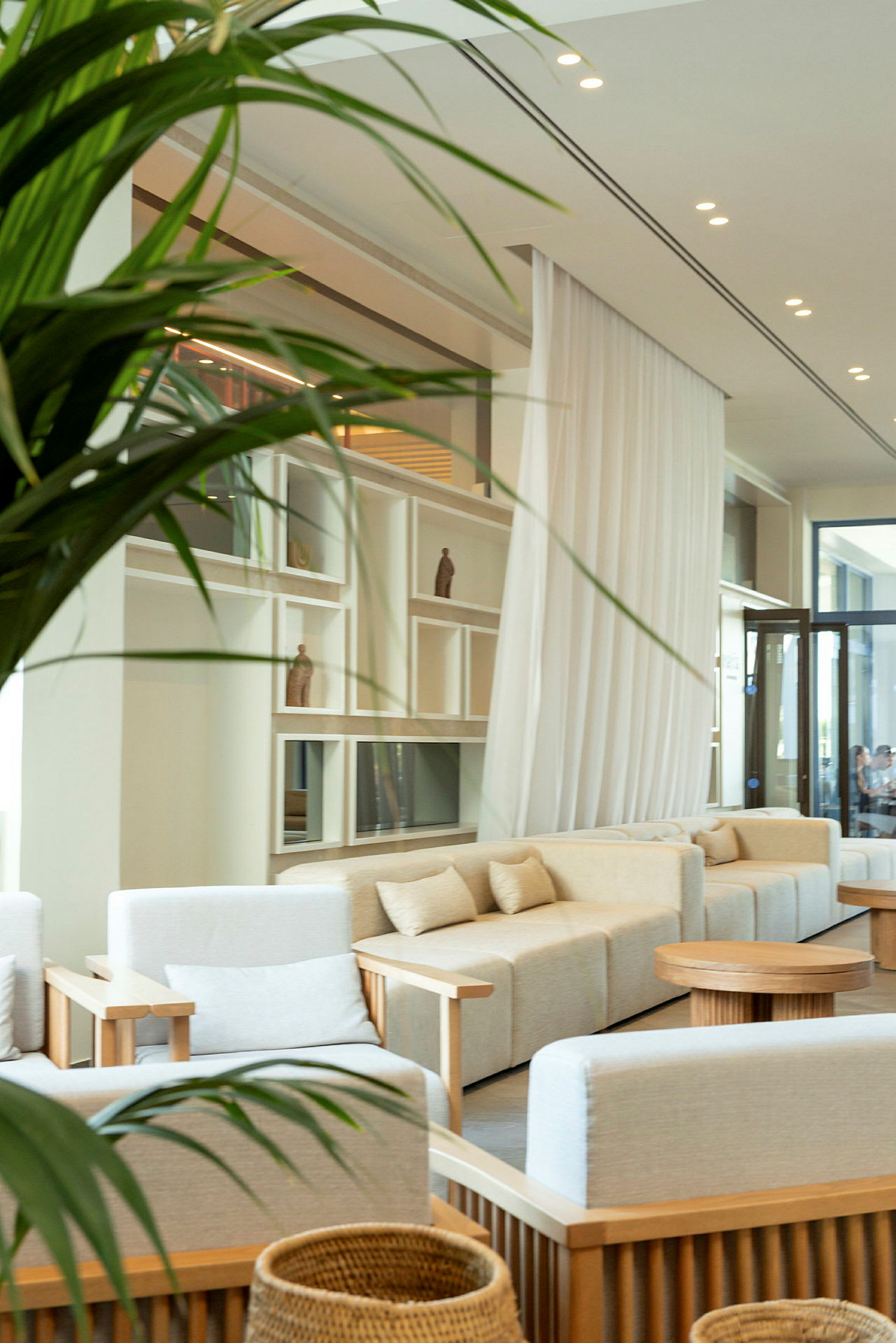 Lys og elegant lobby med komfortable sofaer og stole i neutrale farver, lave træborde og dekorative hylder i baggrunden. (AI-genereret tekst)