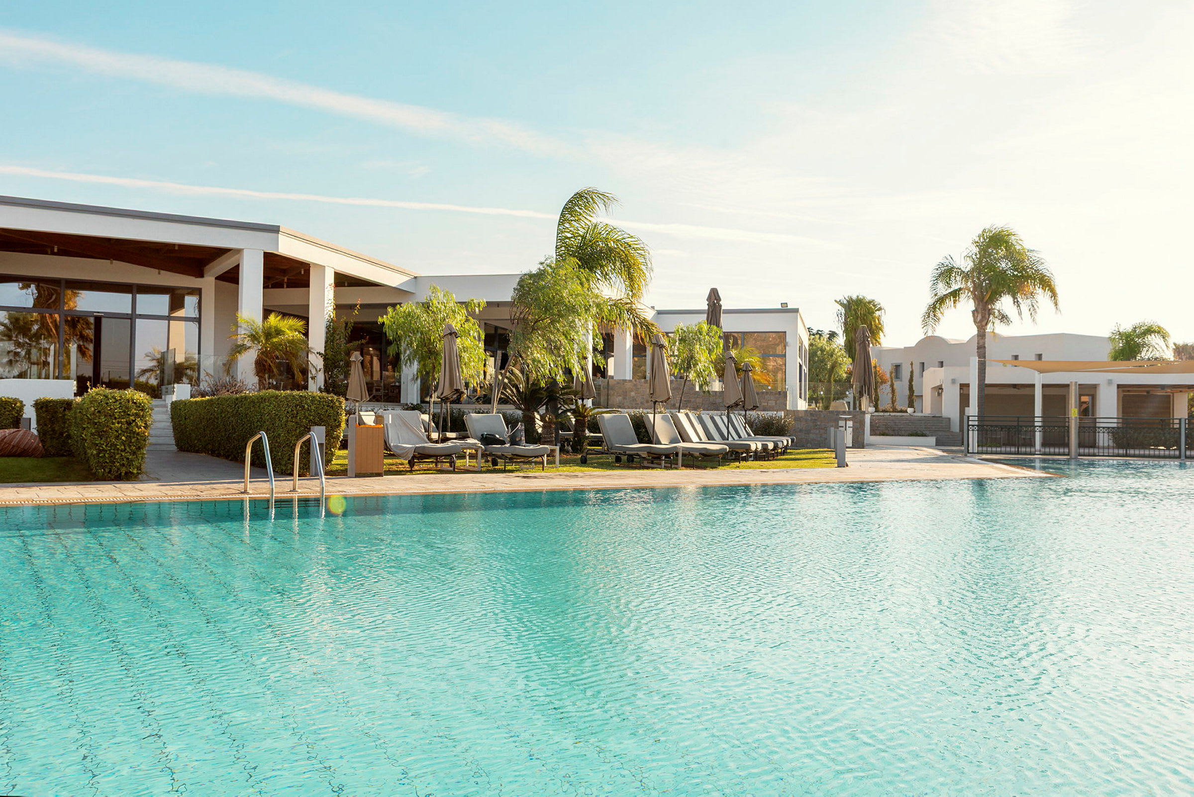Udendørs pool ved et moderne hotel med liggestole og parasoller, omgivet af palmetræer. (AI-genereret tekst)