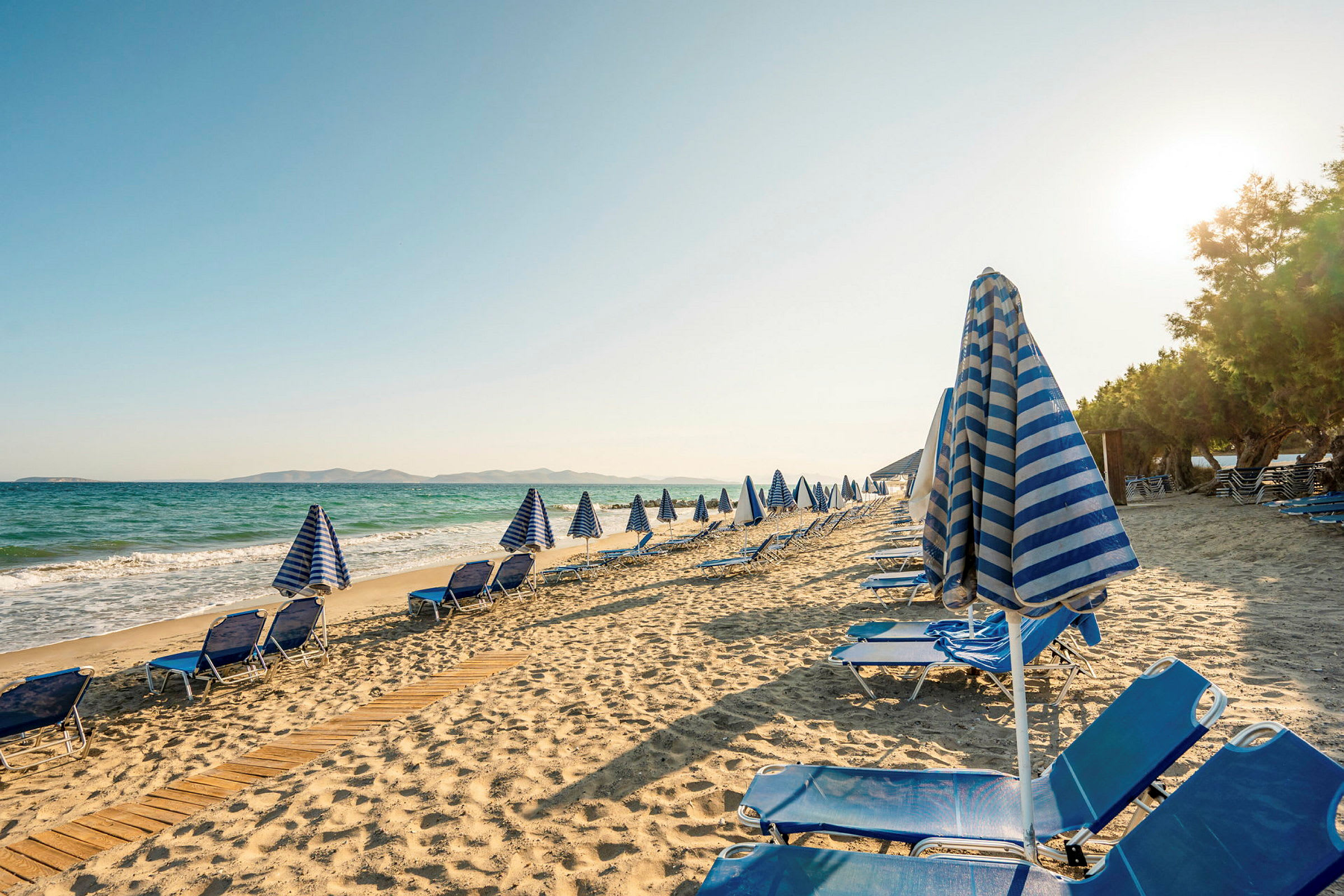 Strand med liggestole og parasoller ved havet. (AI-genereret tekst)