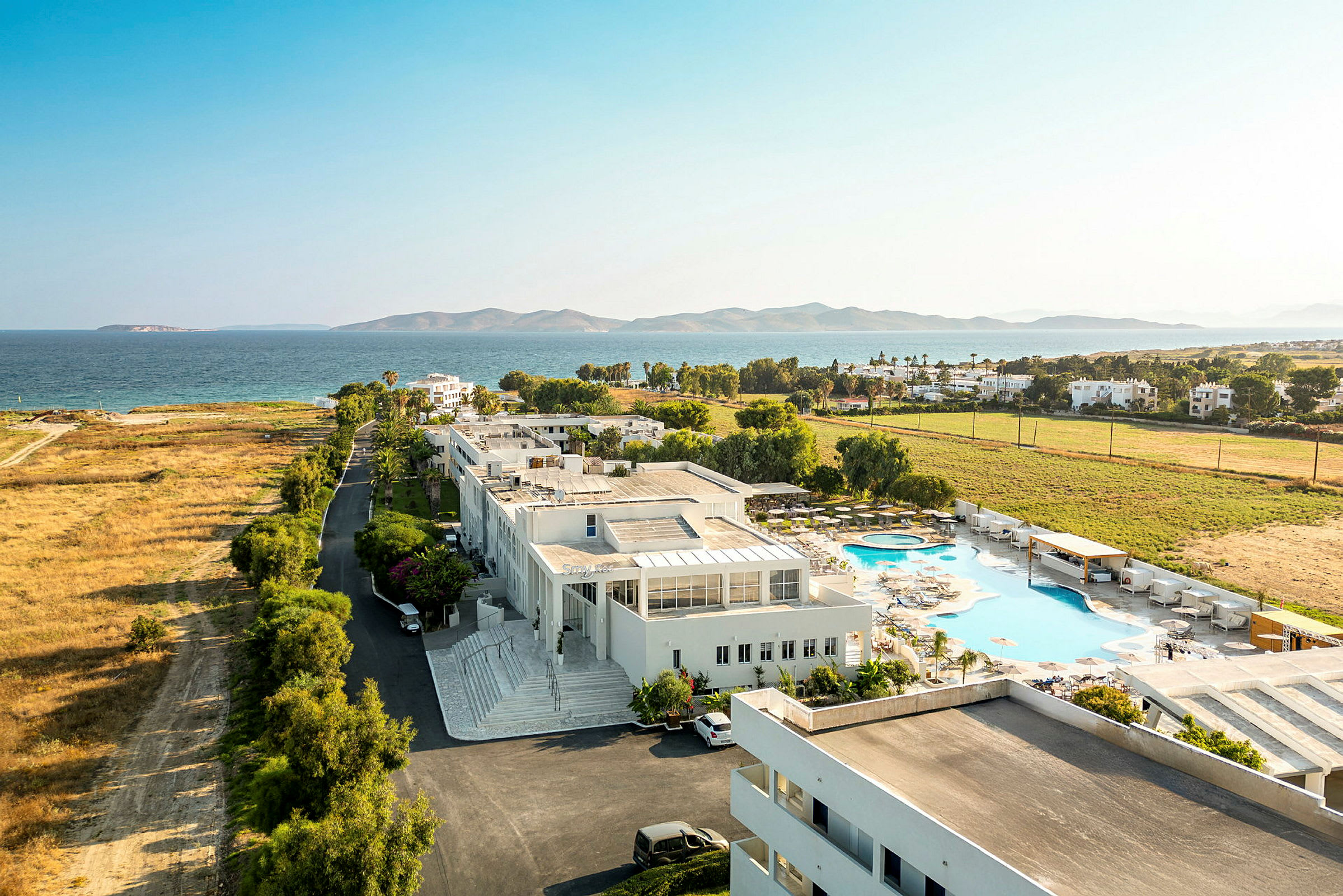 Udsigt fra oven over et feriekompleks nær havet med pool og grønne områder. (AI-genereret tekst)