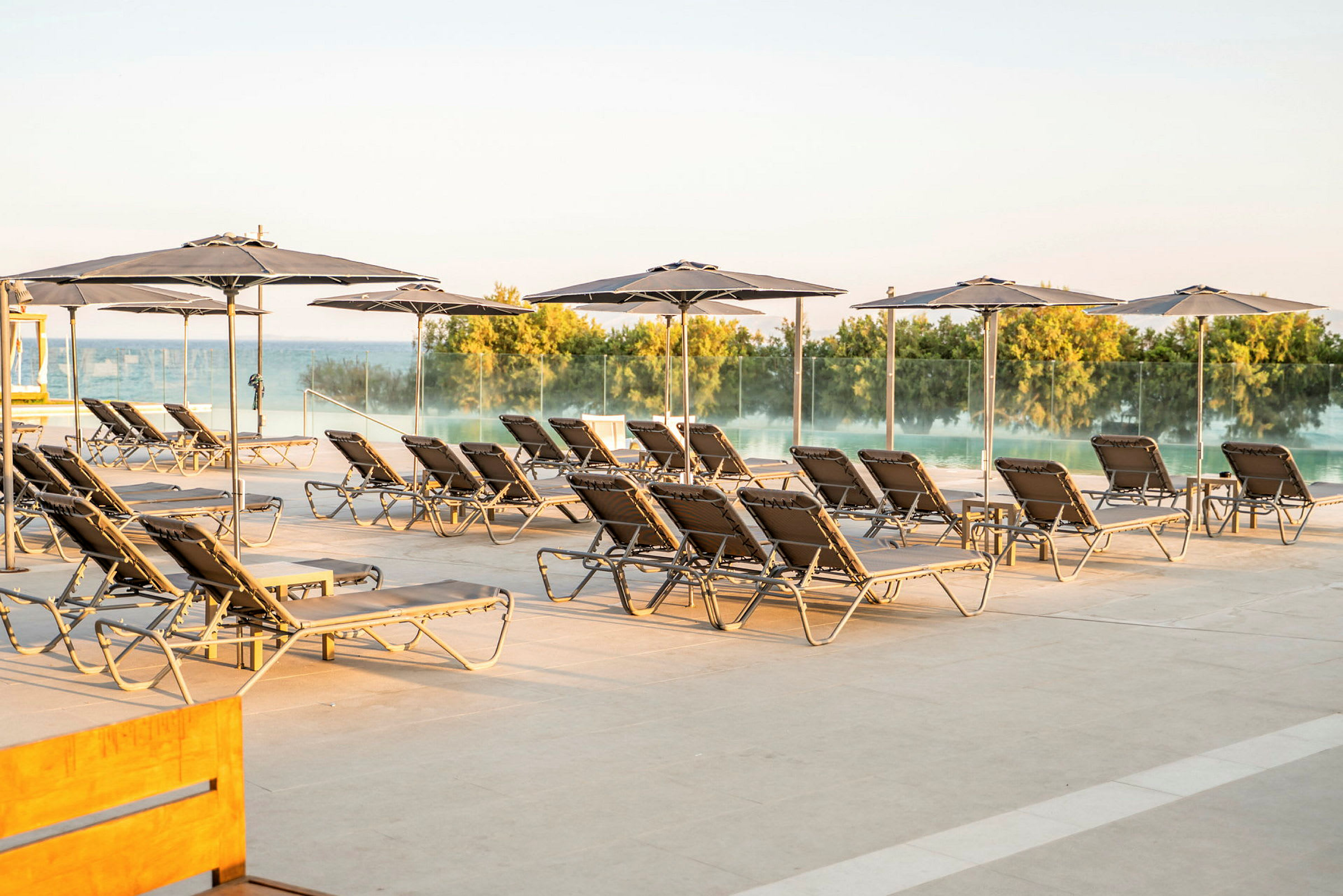 Liggestole og parasoller på en terrasse ved en pool. (AI-genereret tekst)